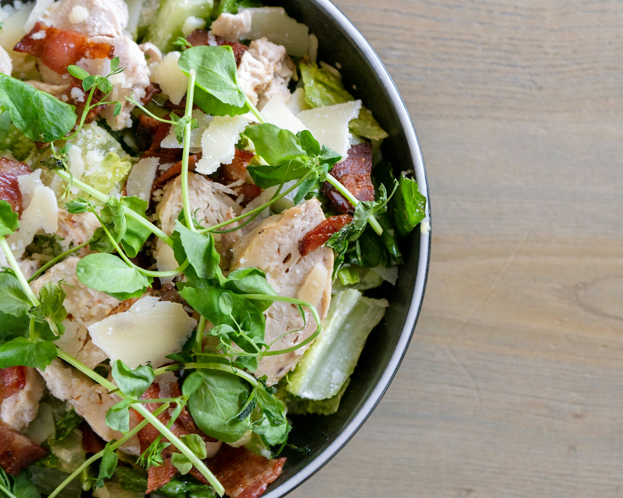 Ein Teller Caesar Salad mit Hähnchenfilet, Speck, Parmesan und Salat. Foto