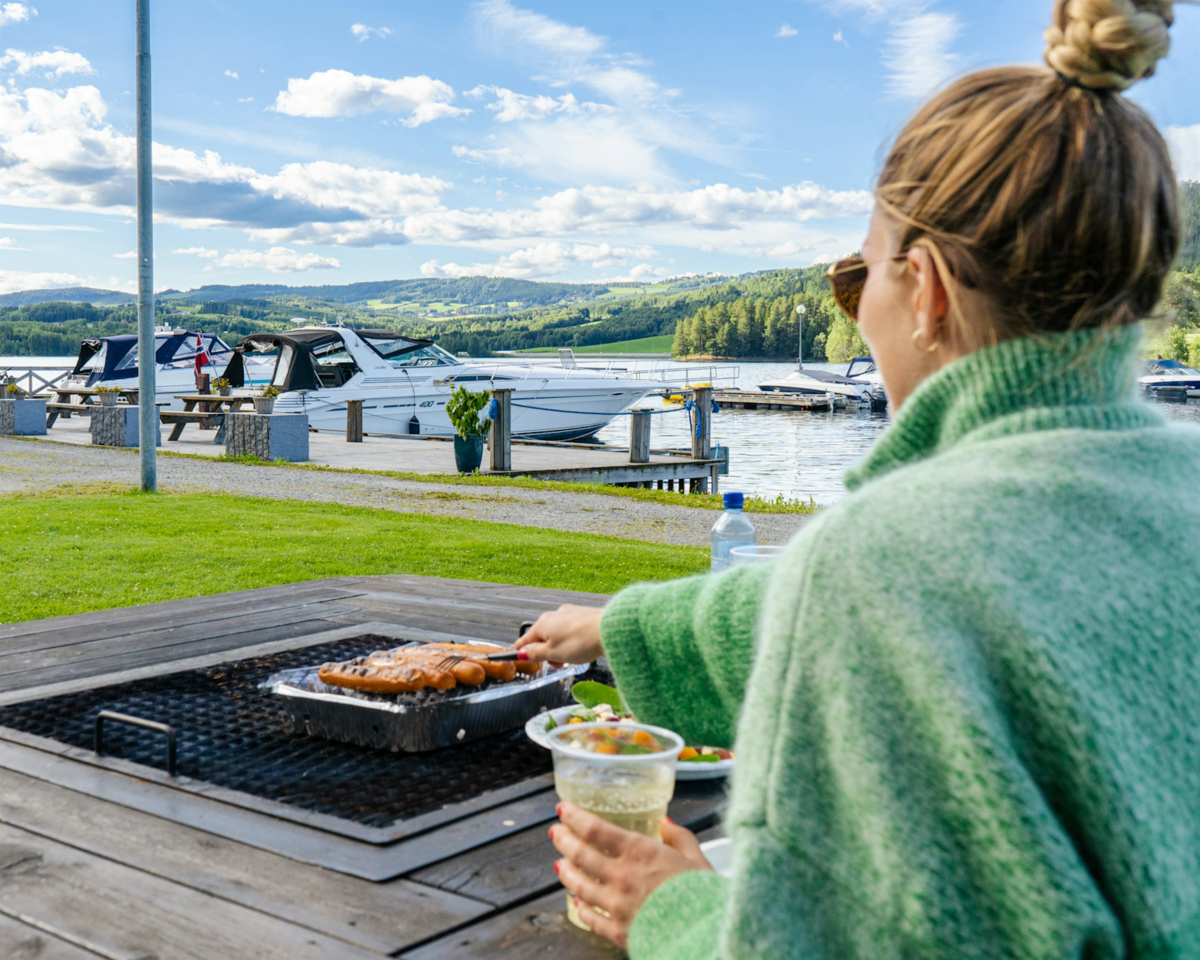 Girl sits barbecuing with a view of Mjøsa and boats. Photo