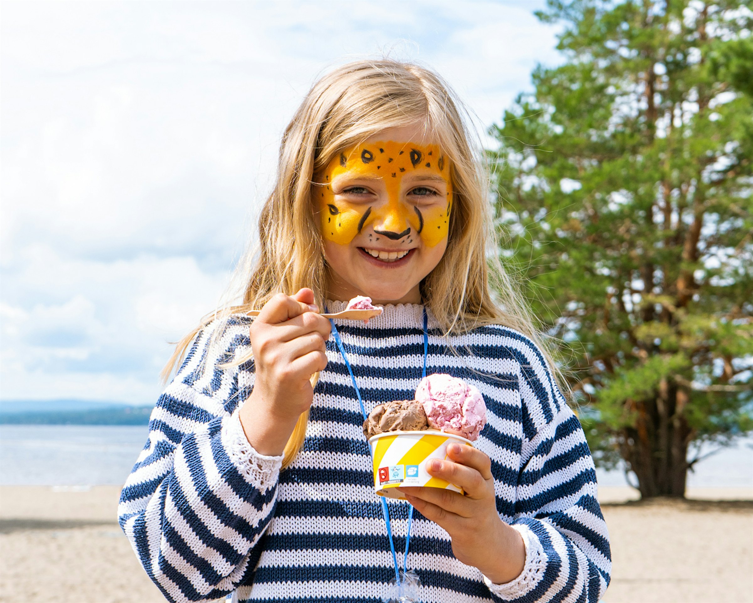 Mädchen hat ihr Gesicht bemalt, isst Eis und lächelt. Foto