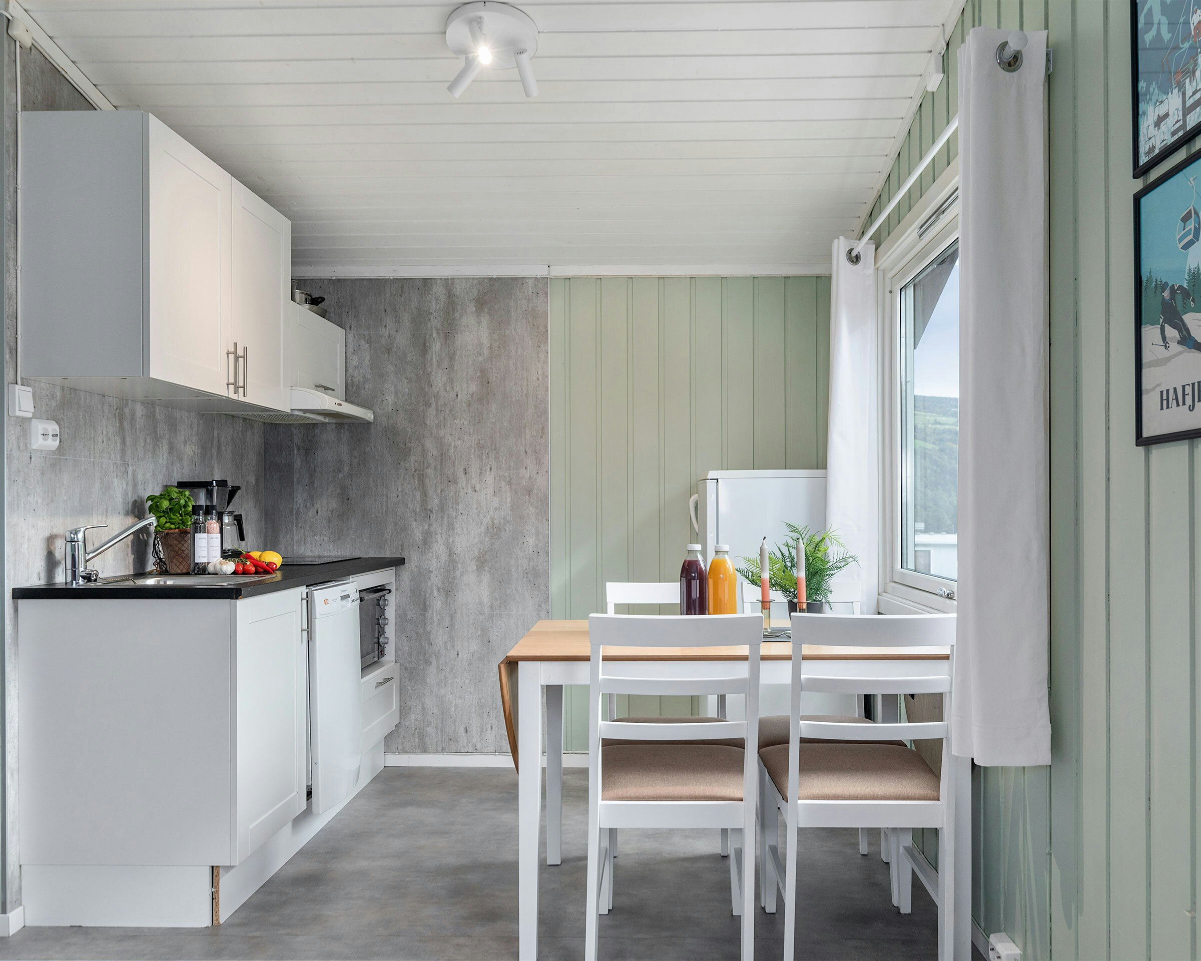 Helle Küche mit hellgrünen Wänden, Gemüse auf der Küchentheke, Esstisch mit Pflanzen, Kerzenständern und Saft. Foto
