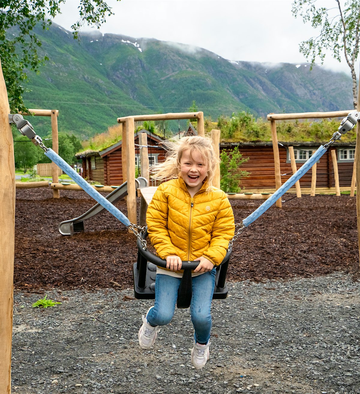 Mädchen erinnert sich auf Spielplatz, mit Bergen im Hintergrund. Foto