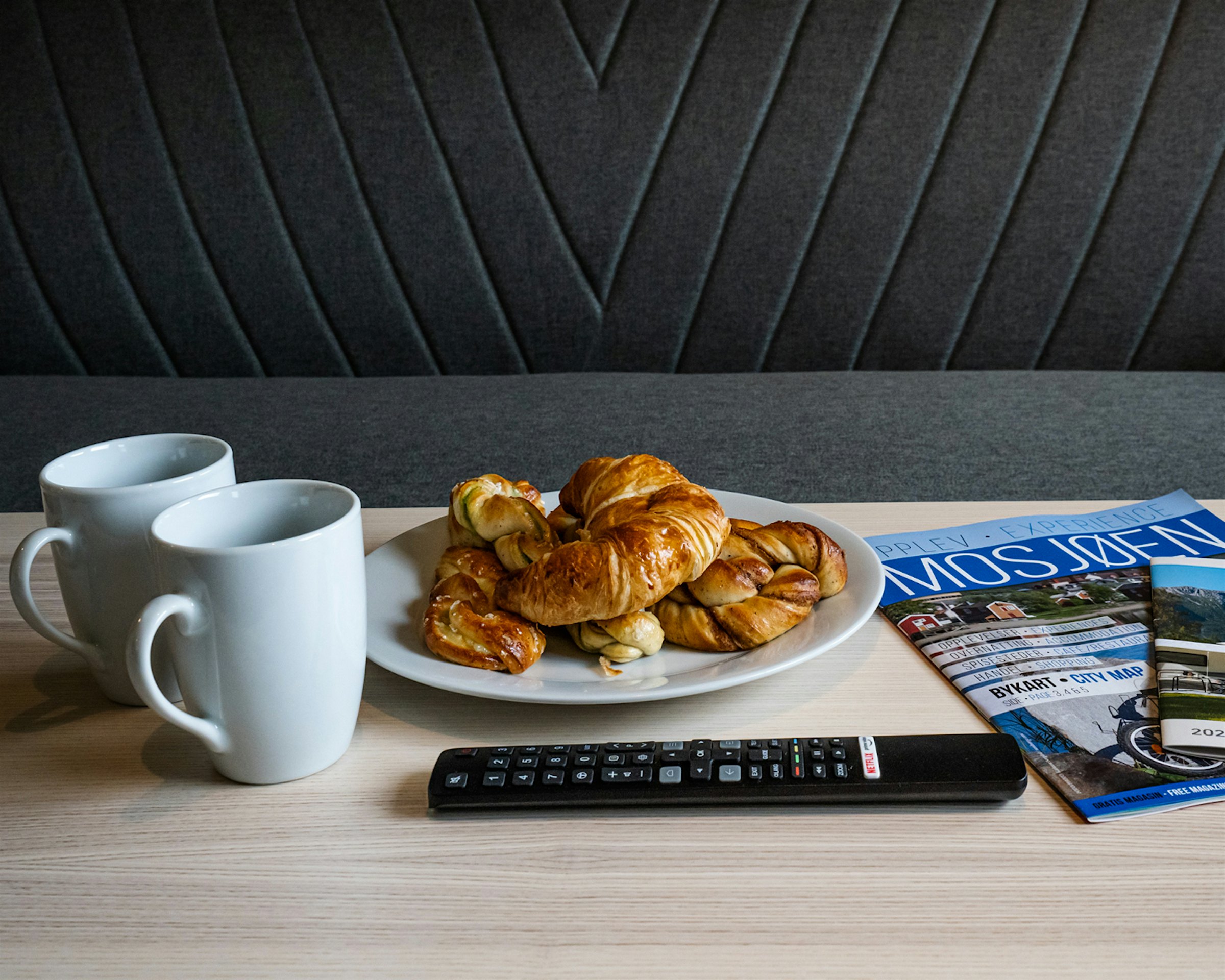 Close-up of two coffee cups, pastries, brochures and remote control. Photo