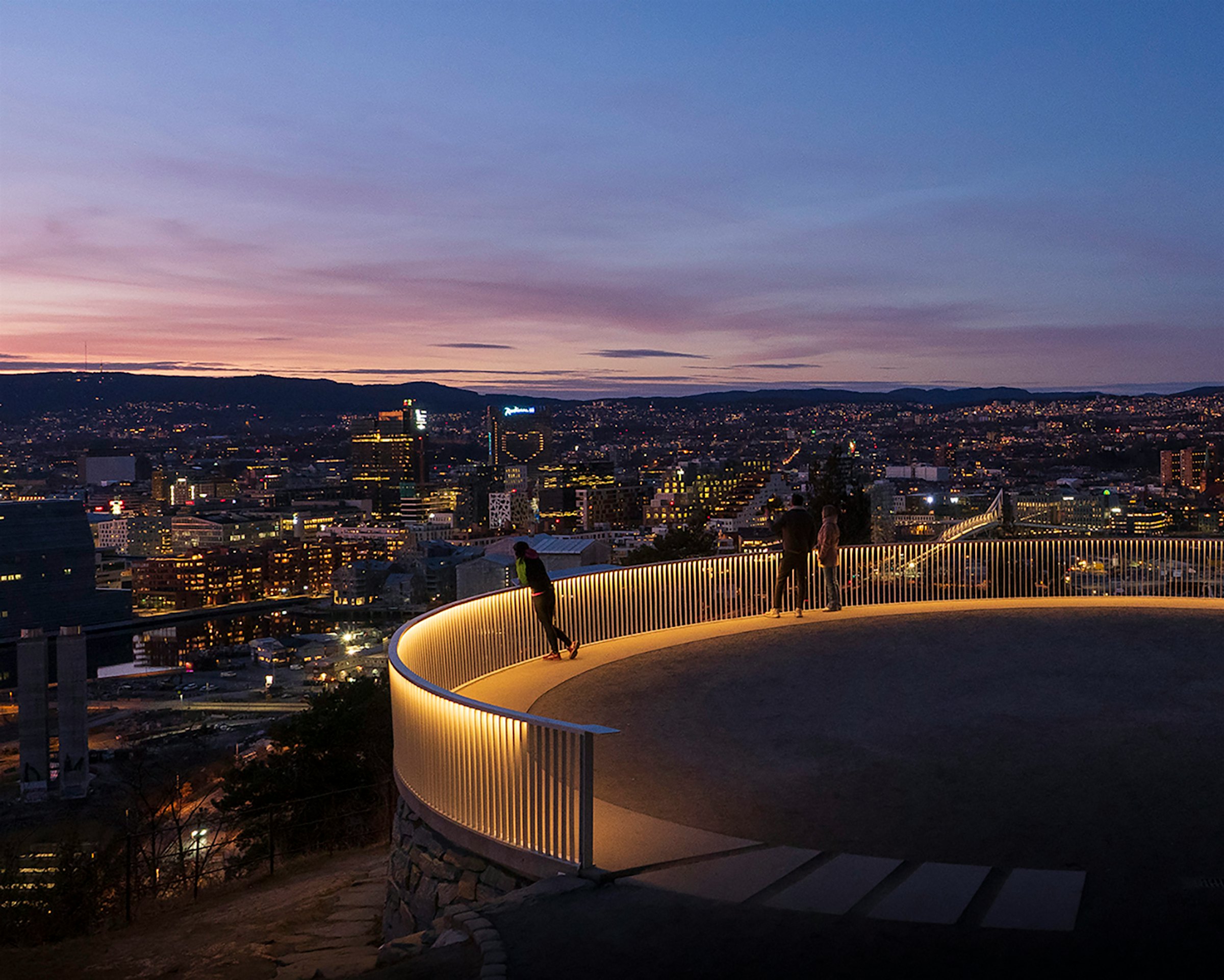 Utsiktspunkt i Ekebergparken med Oslo by i bakgrunnen. Det er etter solnedgang og gjerde lyser, sammen med byen i bakgrunnen.