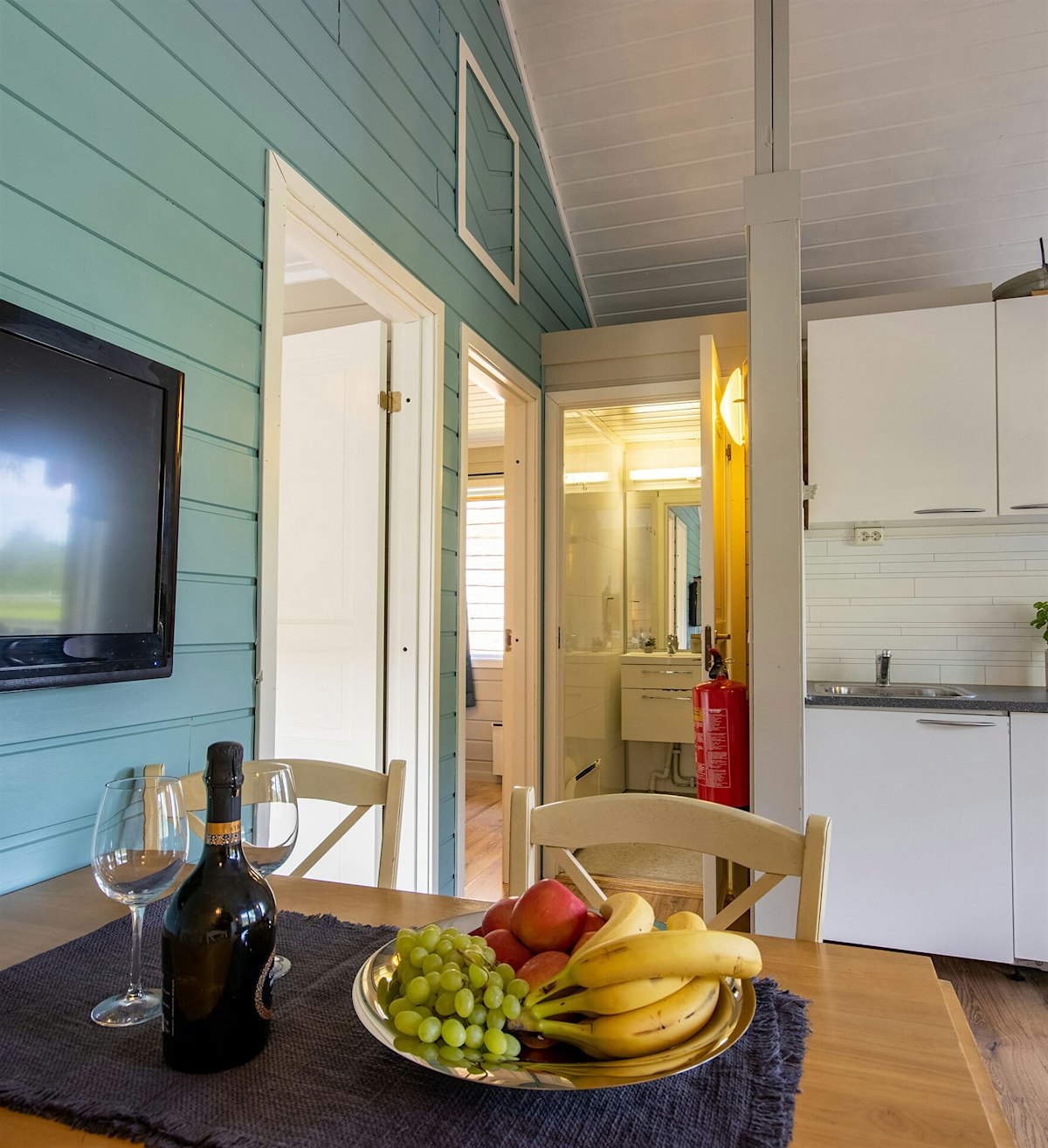 Wohnzimmer mit blauer Kontrastwand, weißer Küche und Esstisch mit Obstteller. Foto