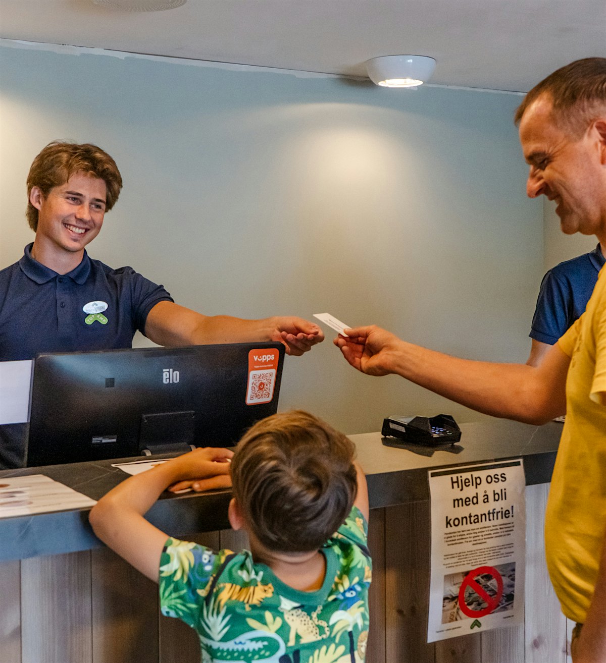 Smiling receptionist gives cards to guests (father and son). Photo