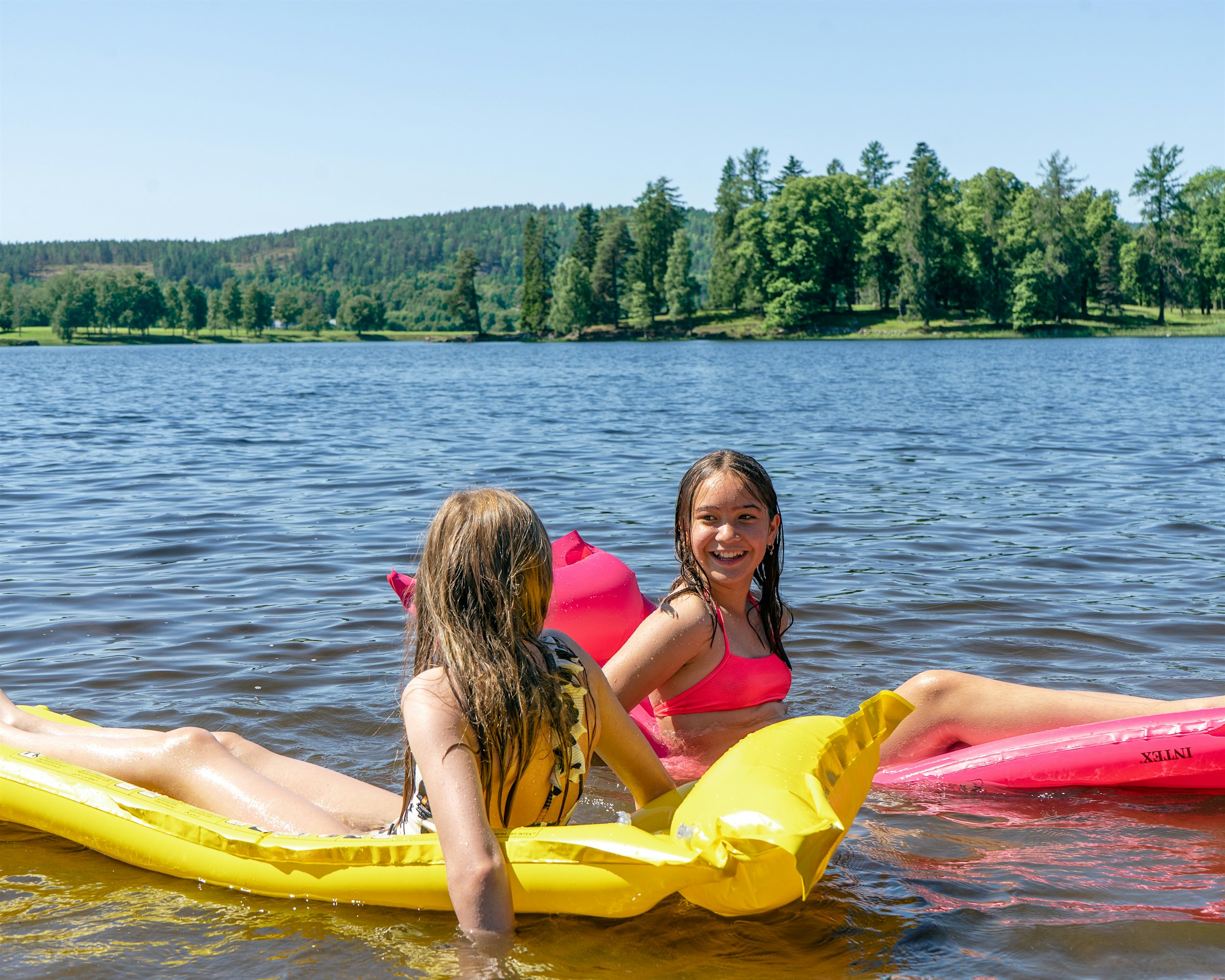 Two girls are each sitting on a floating mattress in the water. Photo