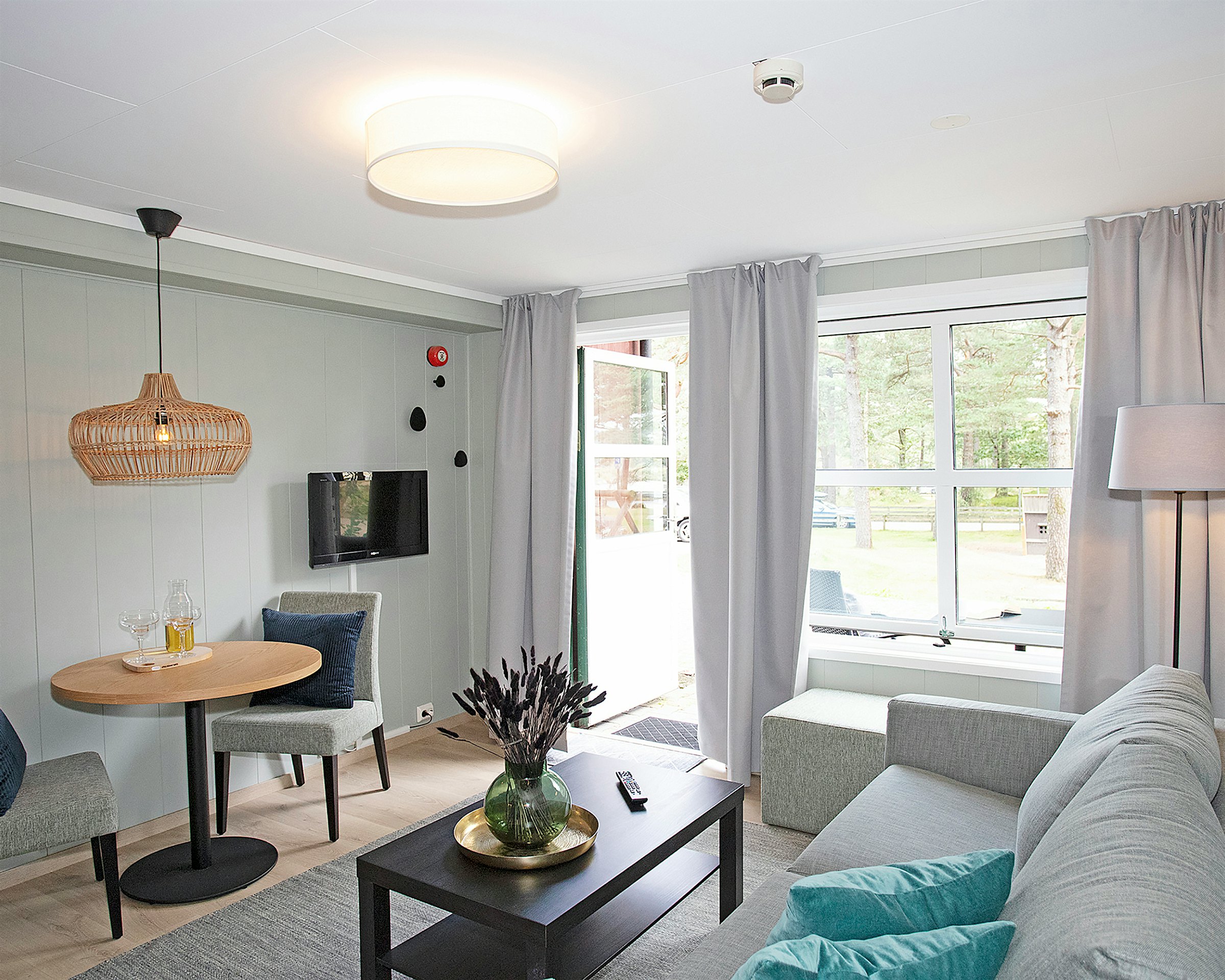 Lys og moderne stue med sofa, spisebord, TV, store vinduer med lange lyse gardinger. Foto