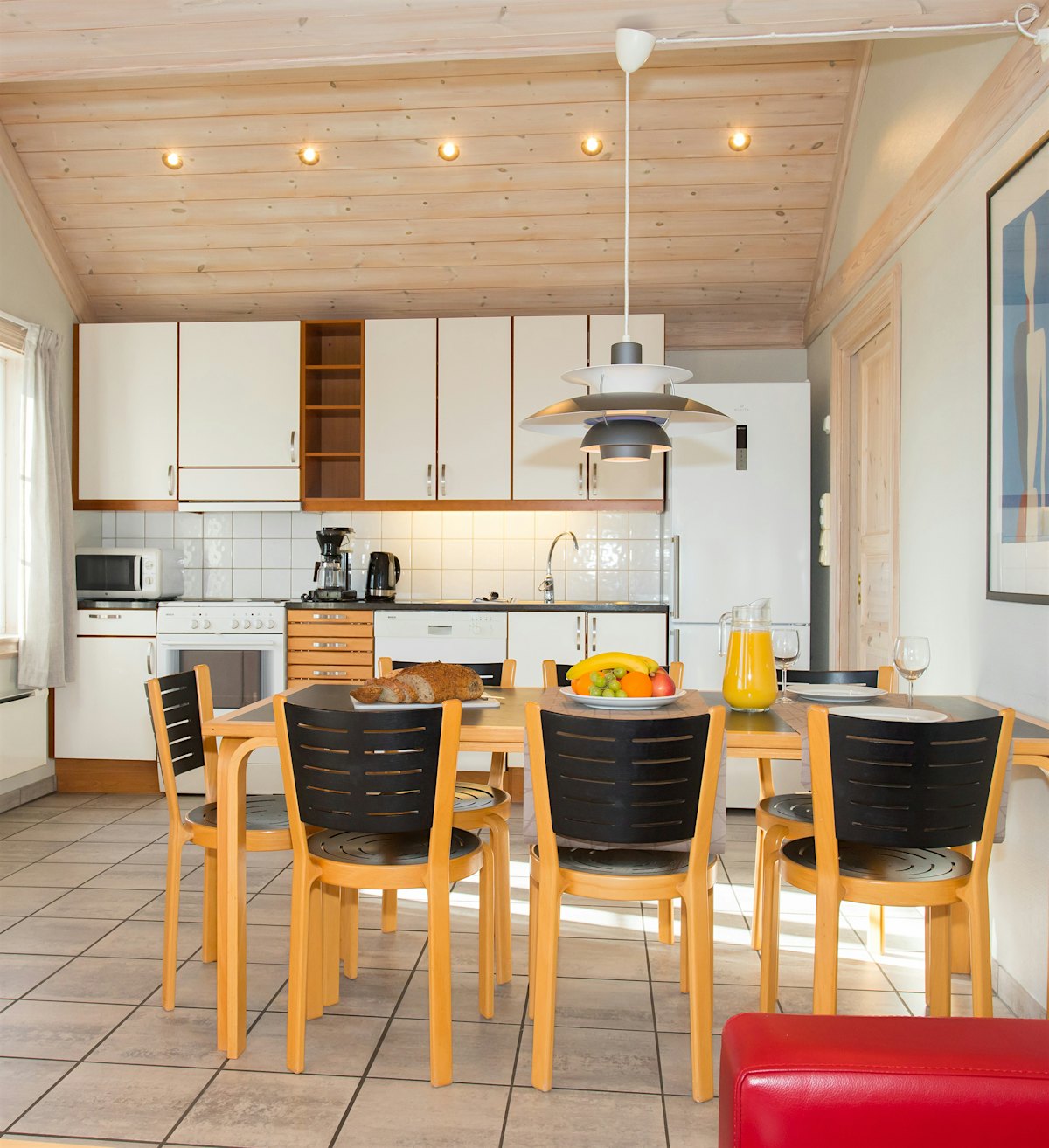 Large open room with kitchen and dining table. The table is covered with fruit platters, bread and drinks. Photo