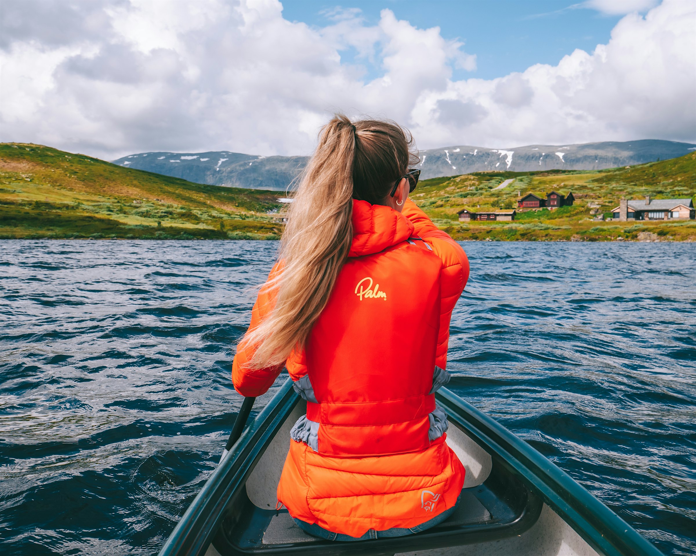 Frau paddelt in einem Kanu auf einem Bergsee, mit Blick auf Berge und Stelzen. Foto