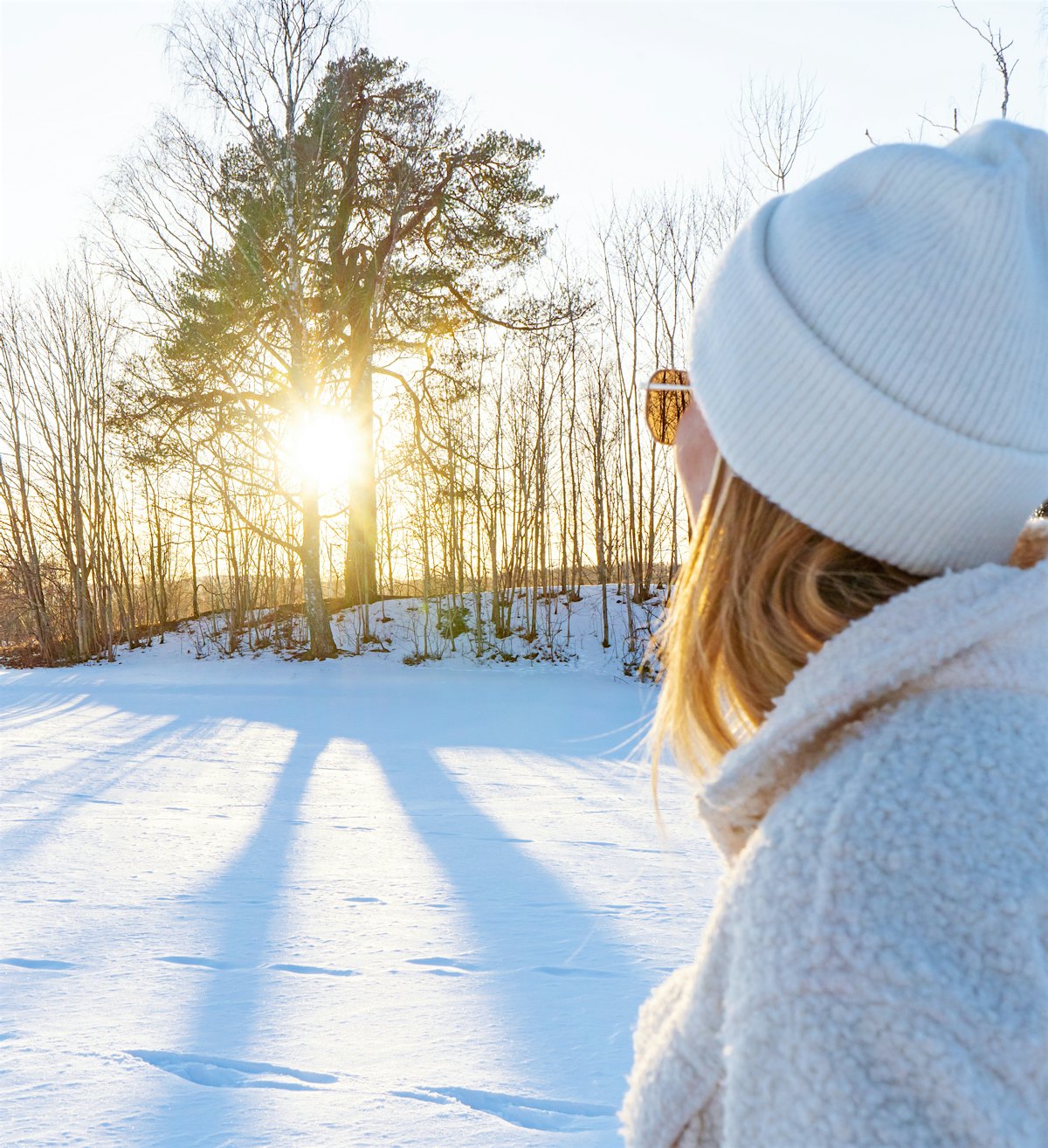 En jente med lue ser mot ettermiddagssolen i vinterlandskap. Foto