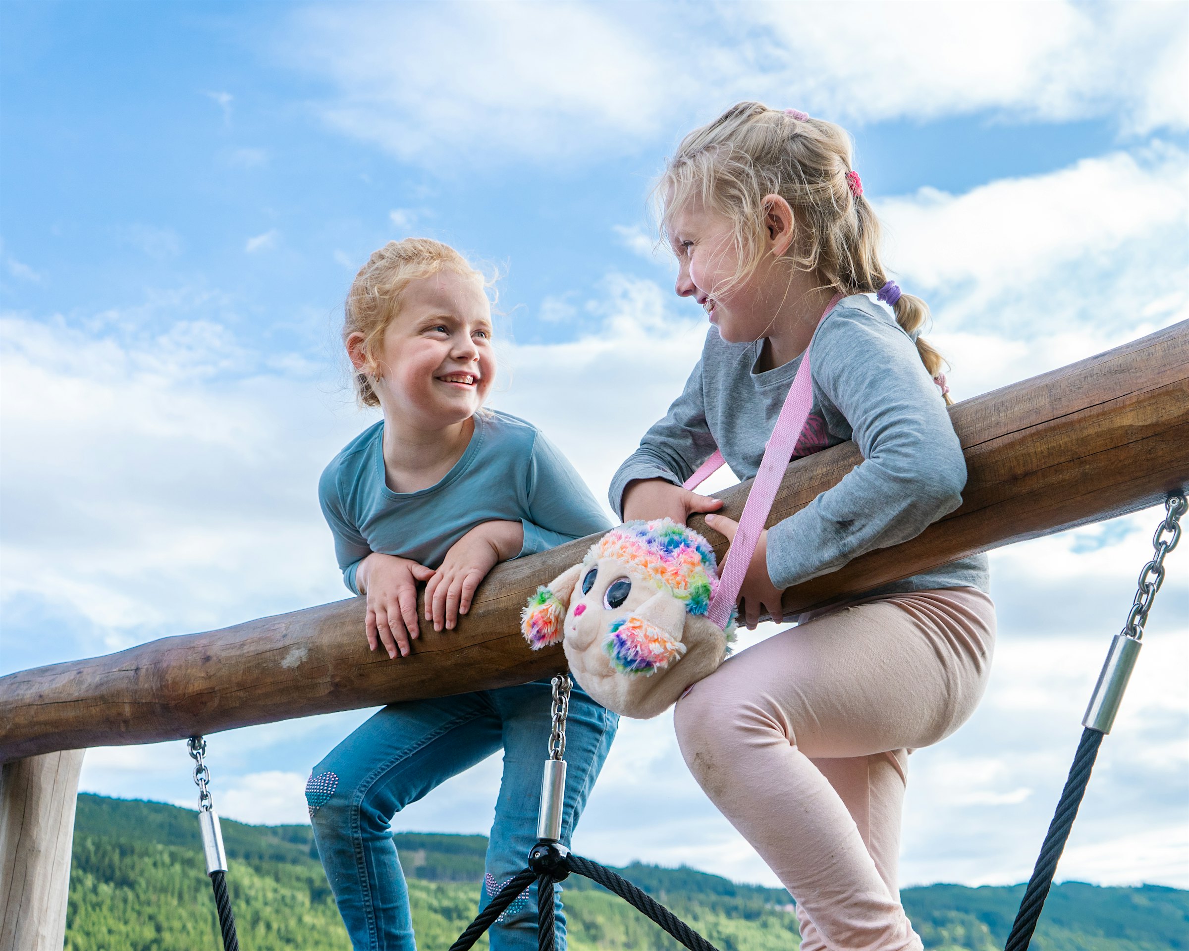 Zwei Mädchen beugen sich über die Kante eines Klettergerüsts und lächeln einander an. Foto