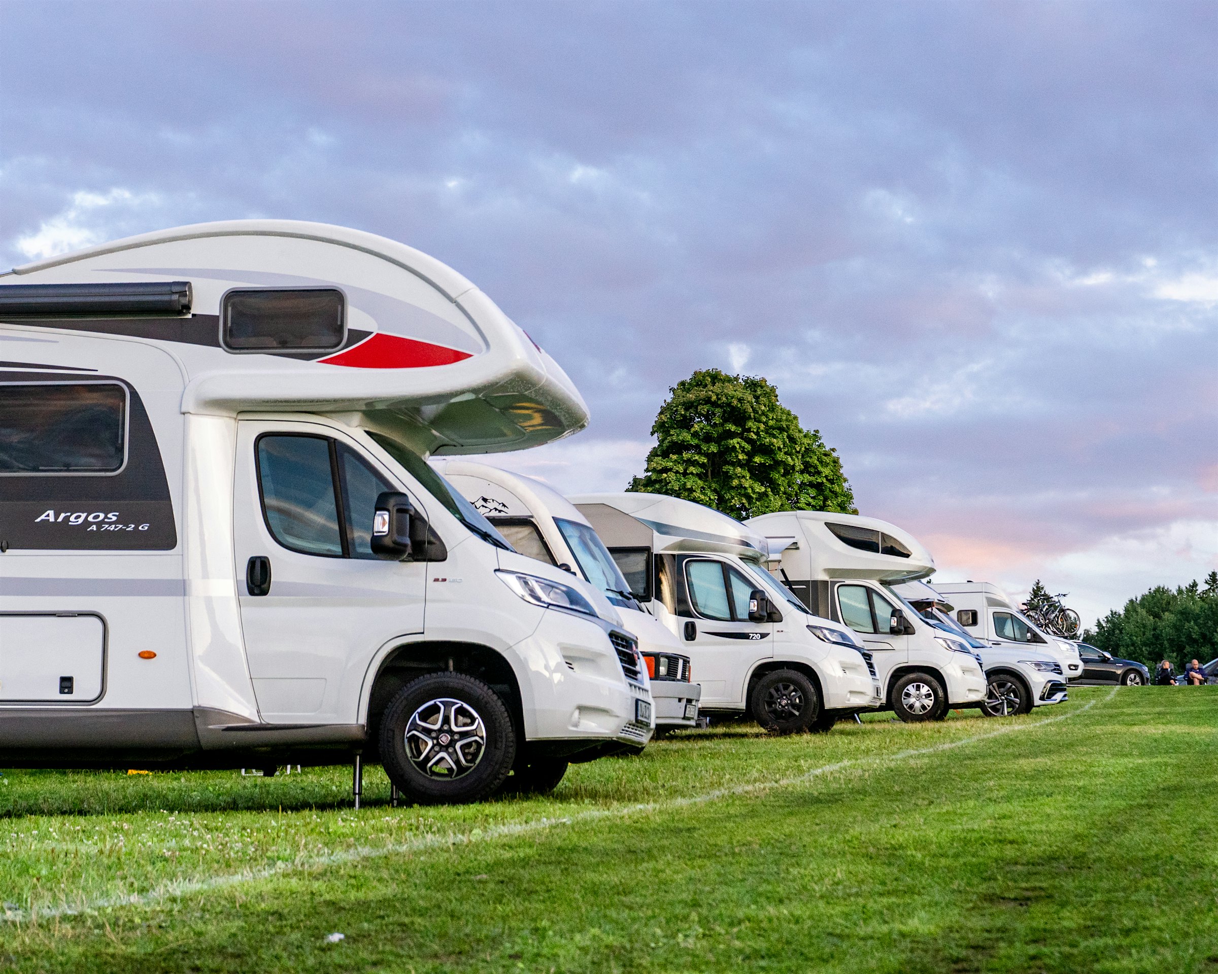 Five motorhomes on a campsite with the sunset in the background. Photo