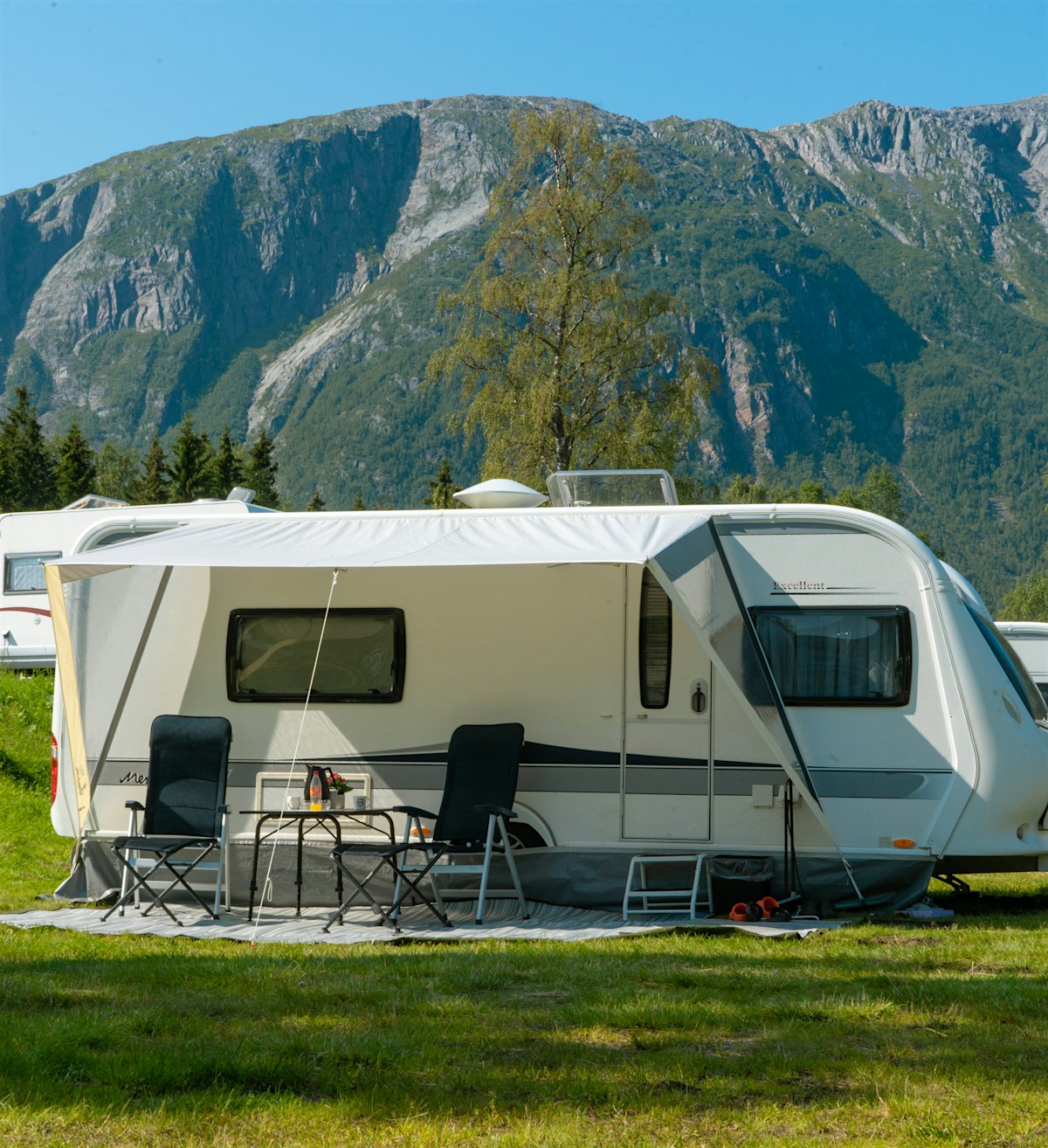 Campingvogn står på campingplass, med høye fjell i bakgrunnen. Foto