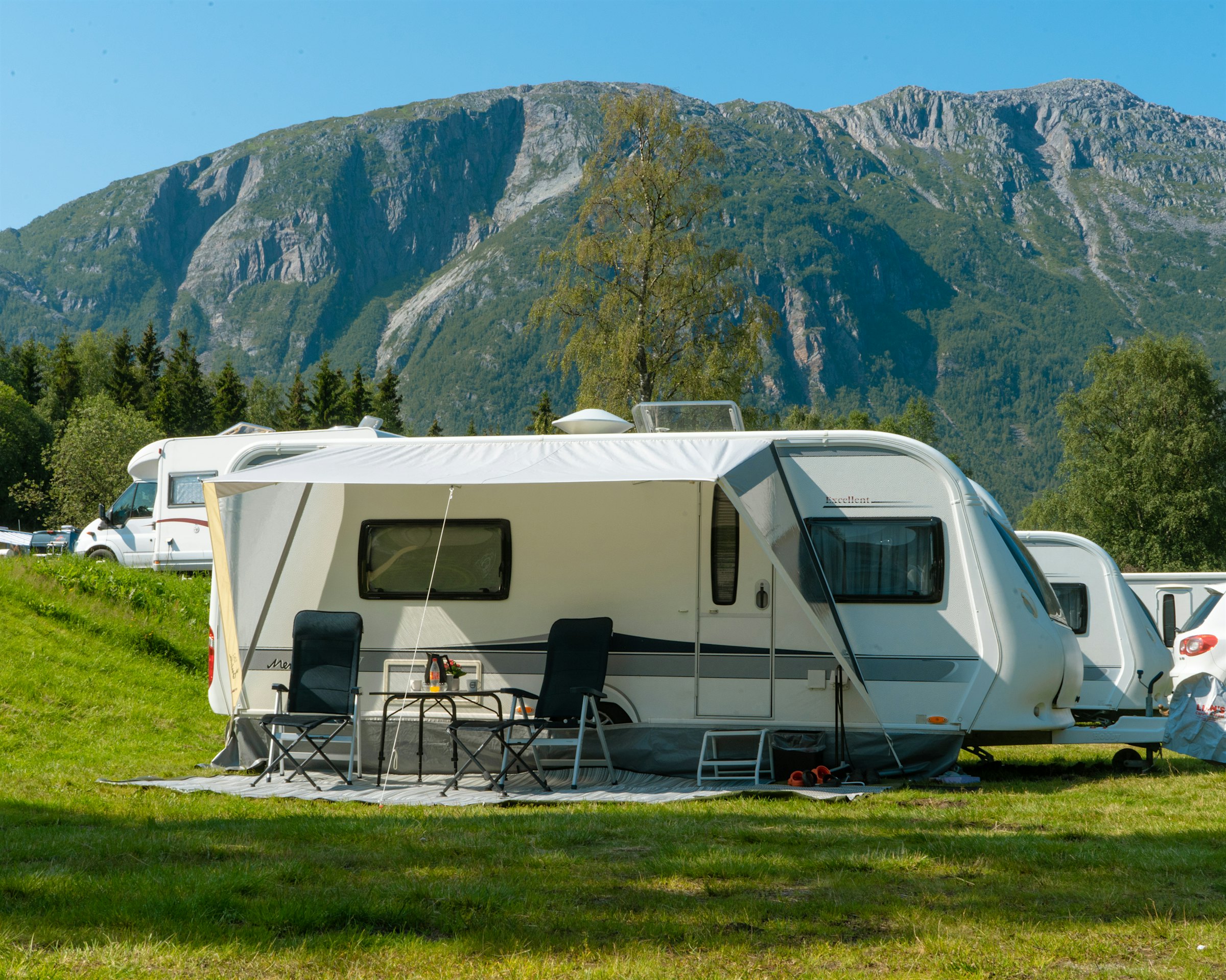 Campingvogn står på campingplass, med høye fjell i bakgrunnen. Foto
