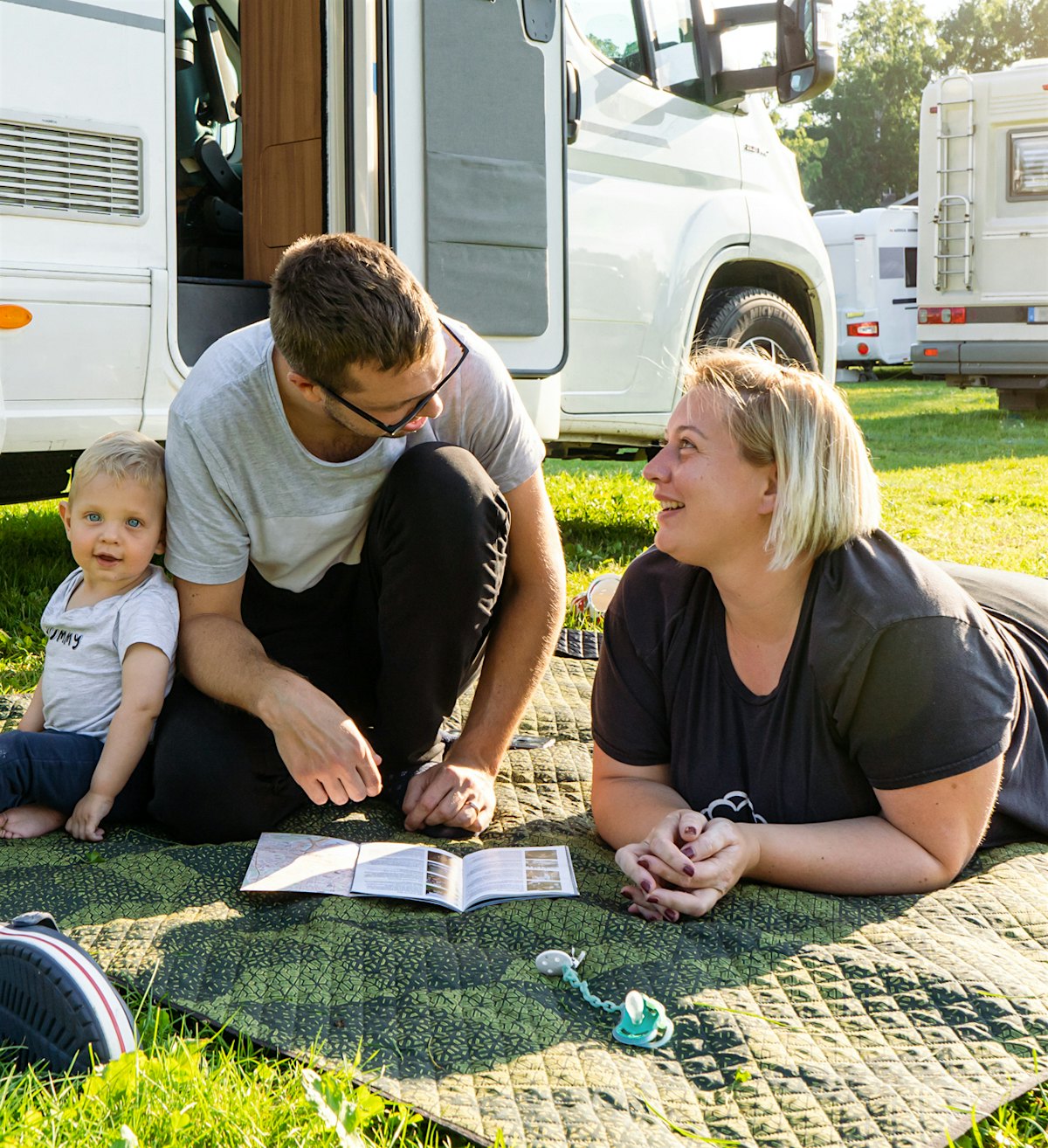Family sits on carpet outside motorhome, looks at map and each other, and smiles. Photo
