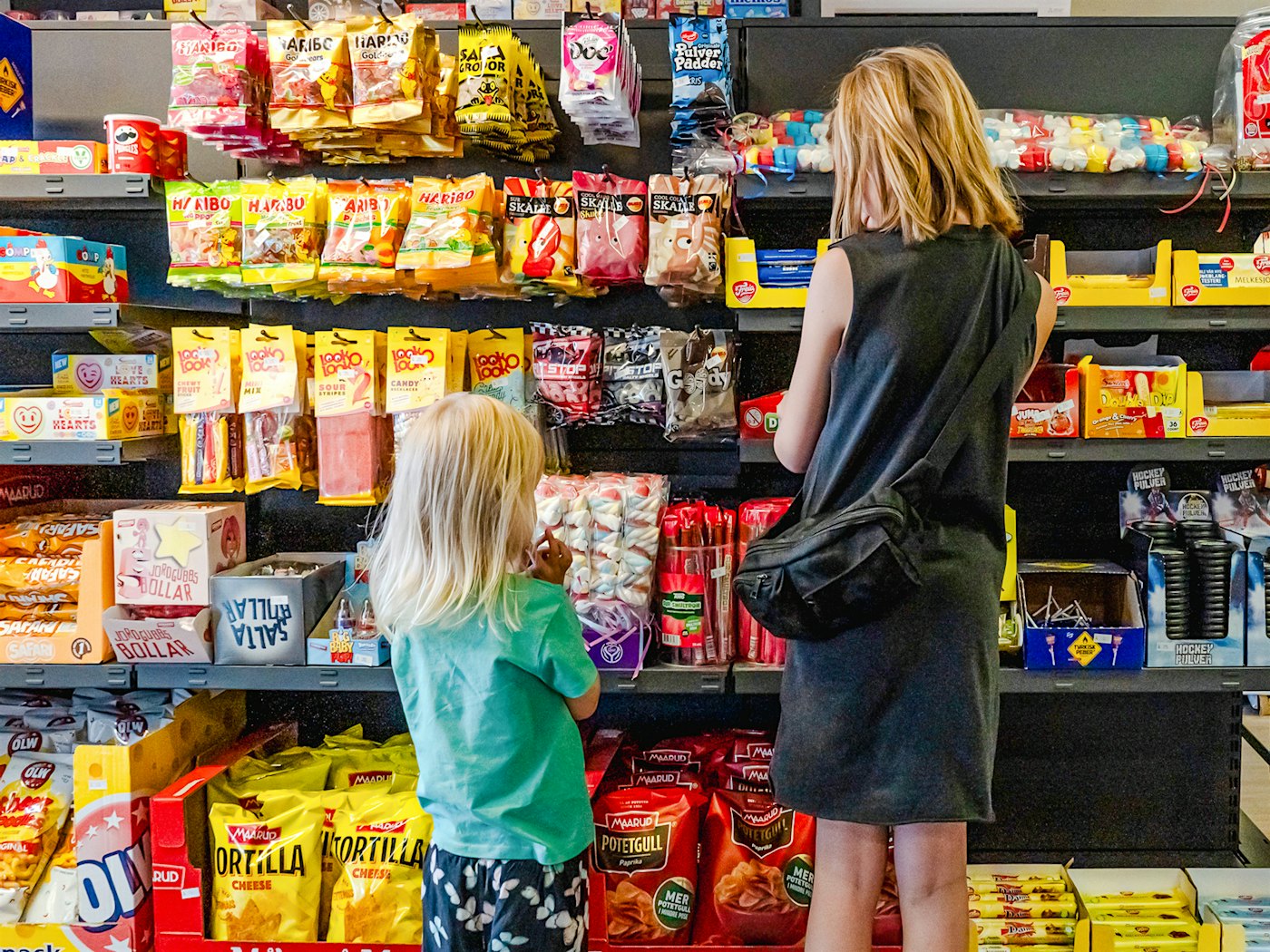 To jenter kikker på en hylle fylt med godteri.