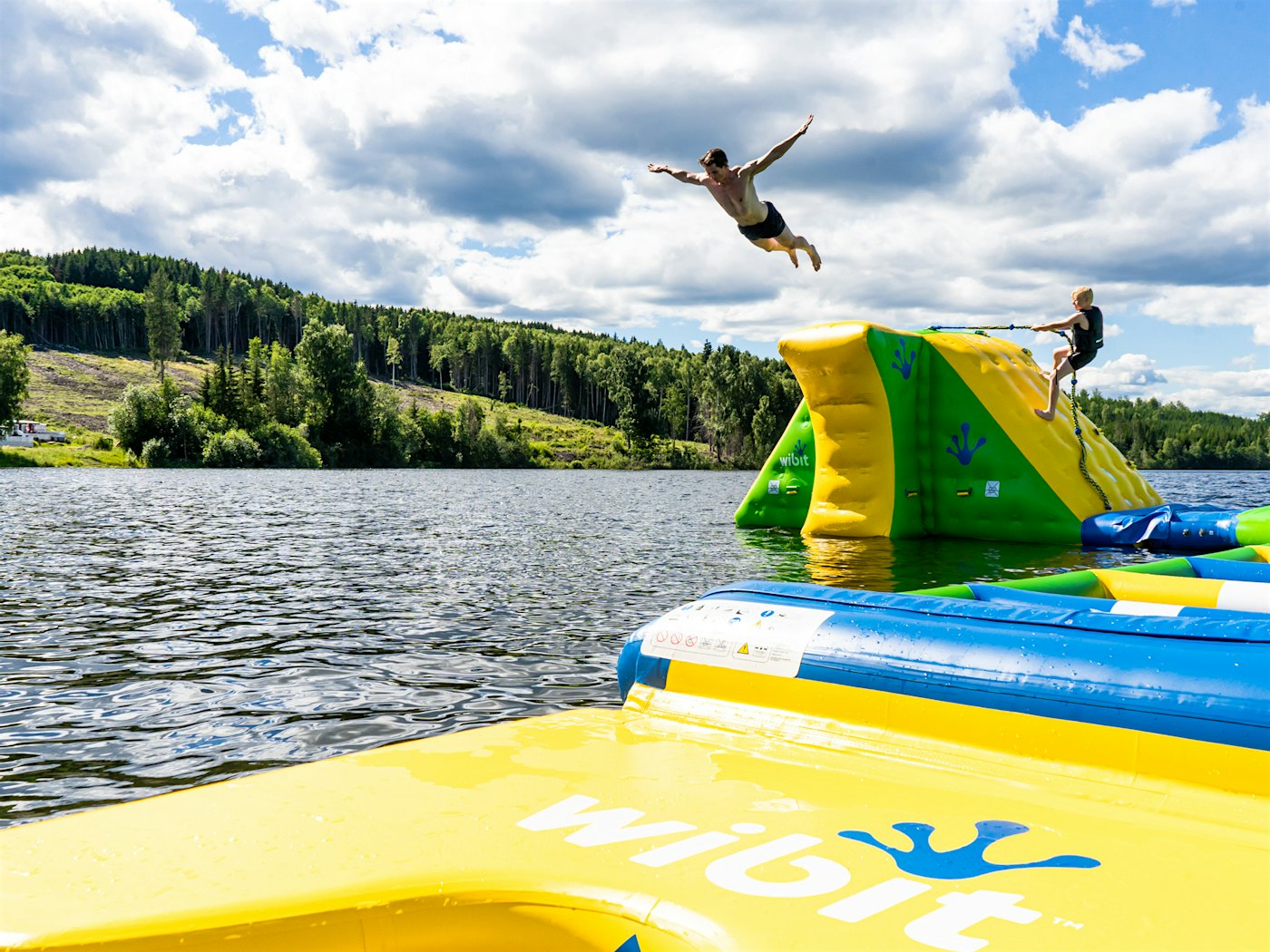 Kinder spielen und vergnügen sich im schwimmenden Wasserpark in Mjøsa, ein Jugendlicher springt von einem Turm. Foto