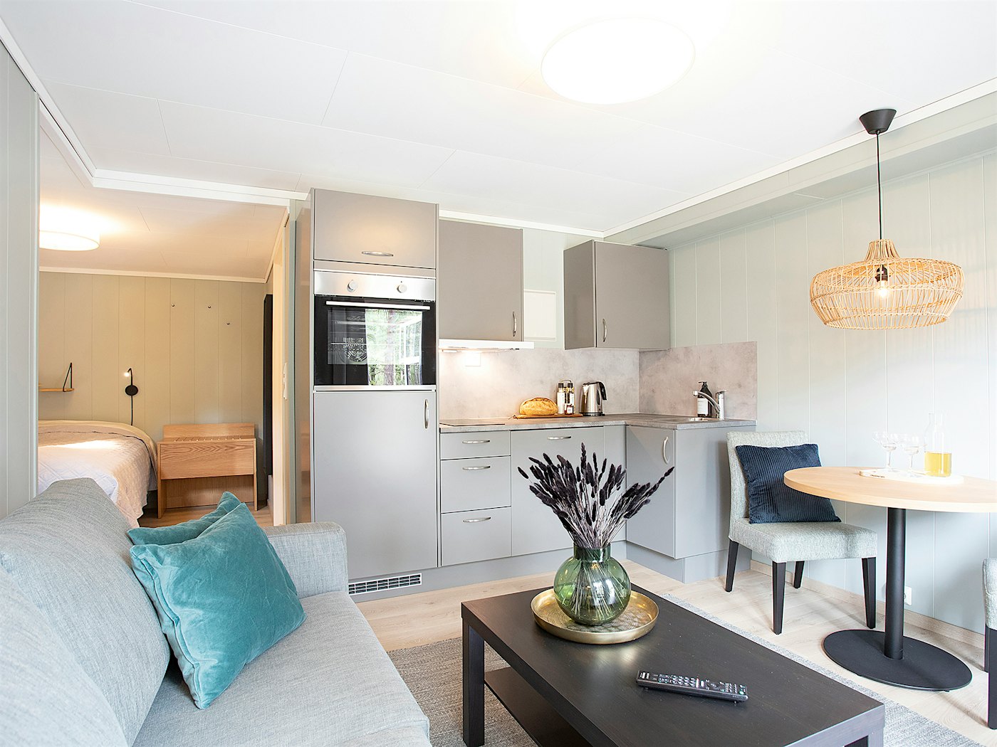 Helles und modernes Studio-Apartment mit Küchenzeile, Esstisch, Sofa und Couchtisch. Doppelbett im Hintergrund. Foto