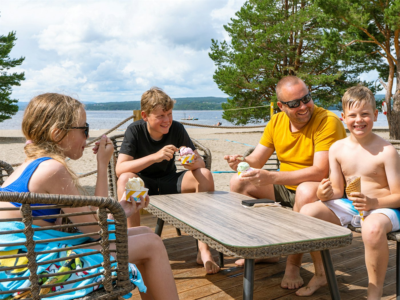 En jente, to gutter og en mann sitter i strandklær rundt et bord på uteservering og spiser is.