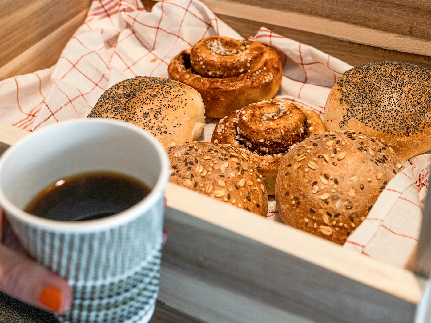 Holzkiste mit Zimtschnecken und Brötchen, Kaffeetasse im Vordergrund. Foto