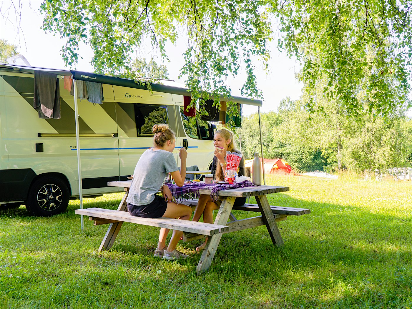 Two girls have breakfast outside their camper. Photo