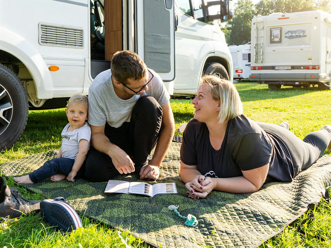 Family sits on carpet outside motorhome, looks at map and each other, and smiles. Photo