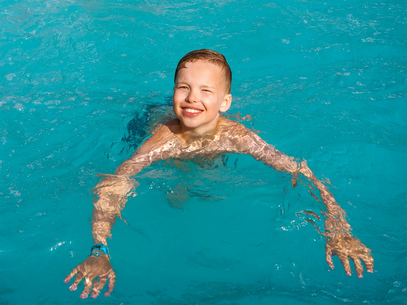 Gutt smiler mot kamera og svømmer i basseng.