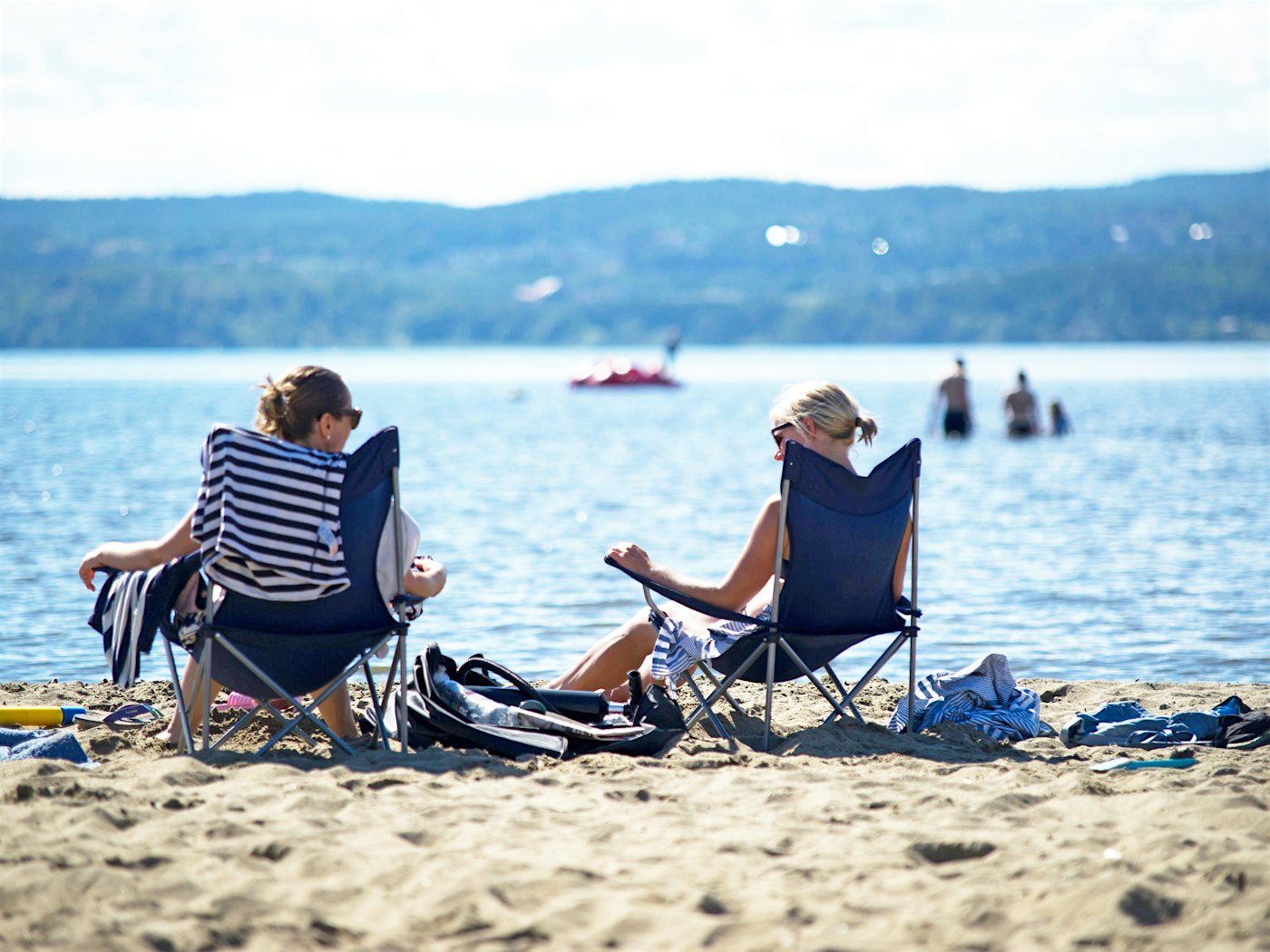 To damer sitter vendt fra kamera i strandstoler på stranden og ser utover vannet.