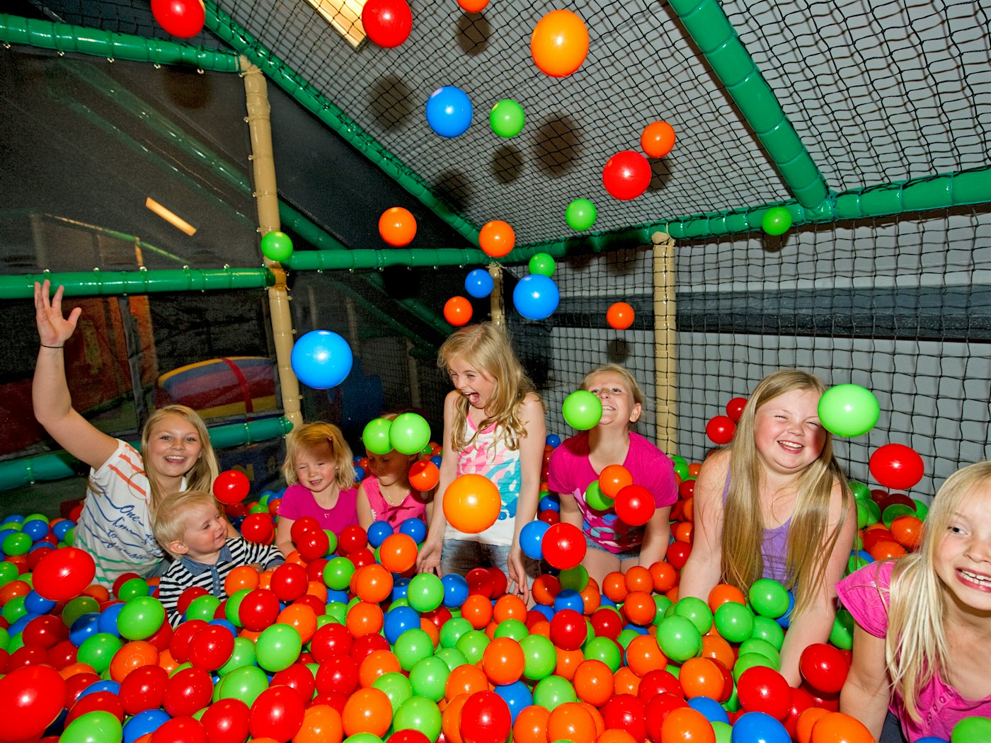 Barn i et ballrom kaster baller høyt opp i luften og ler.