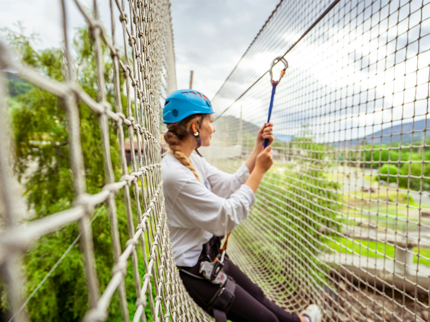 Kvinne med klatreutstyr lener seg i et nett  og ser utover utsikten.