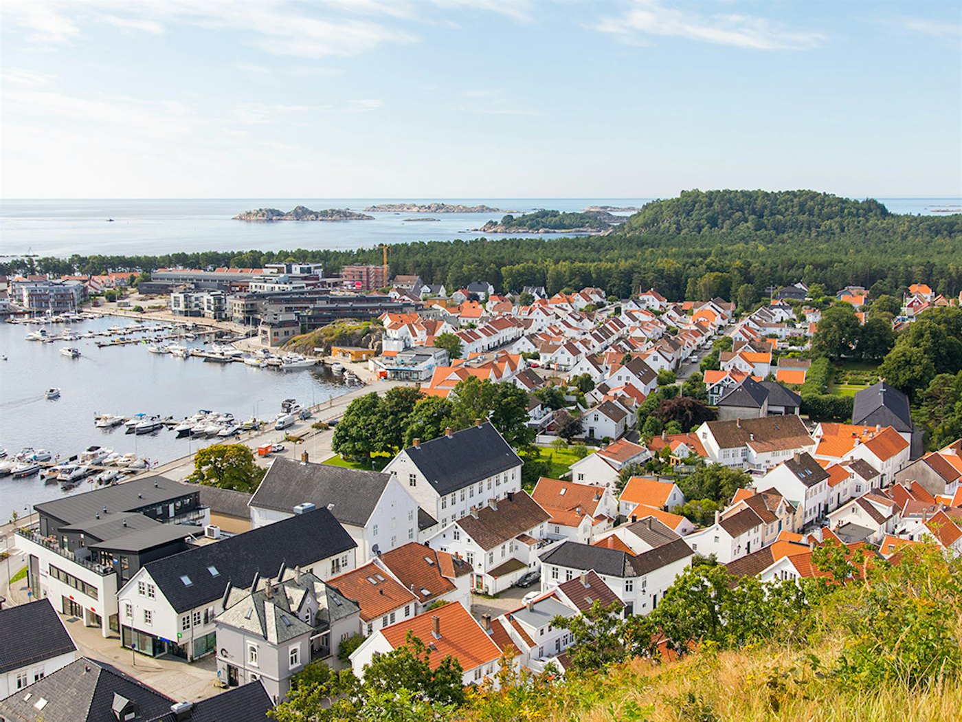 Überblick über Mandal mit vielen weißen Holzhäusern, dem Hafen und Furulunden. Foto