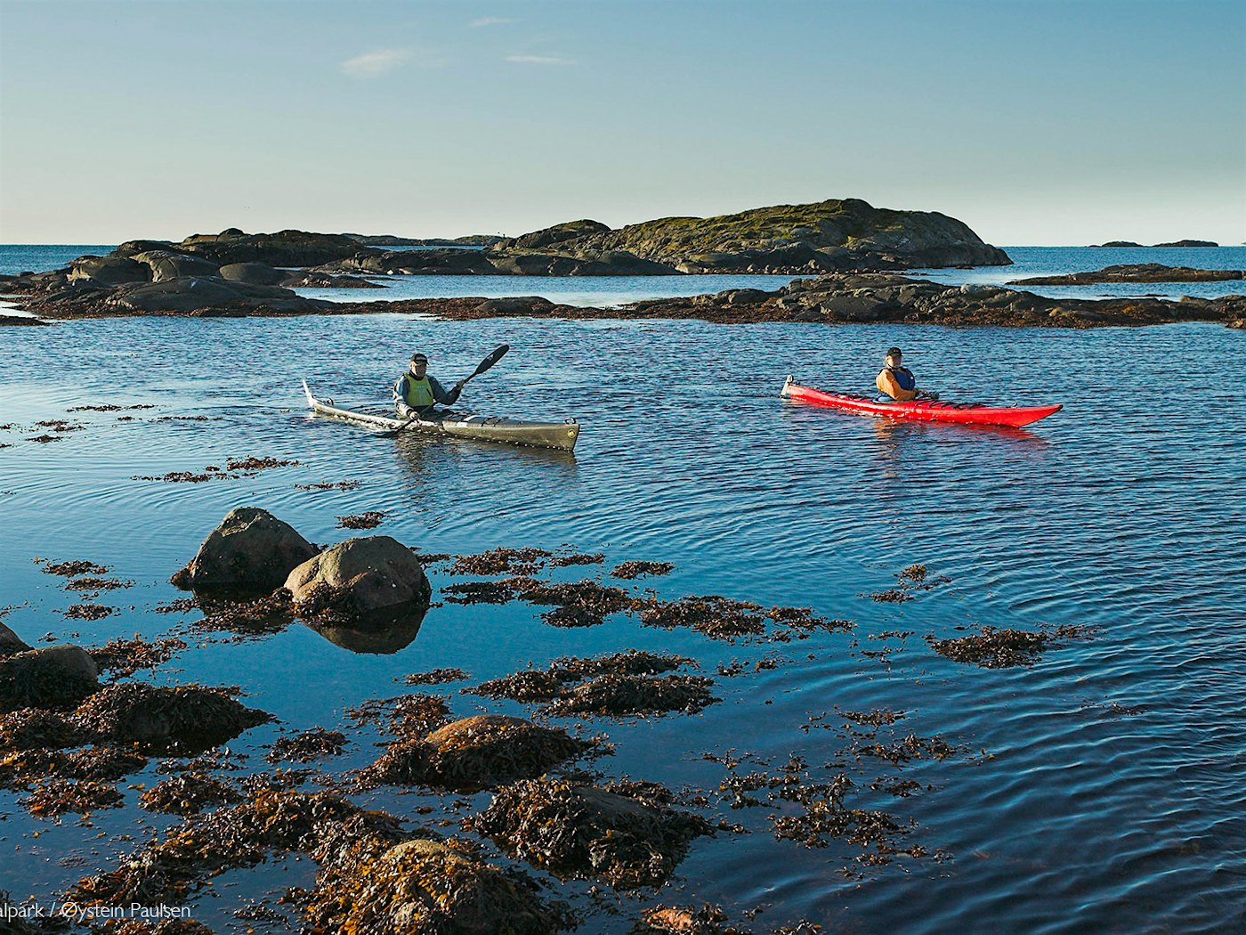Two kayakers on the sea, with rocky cliffs around. Photo