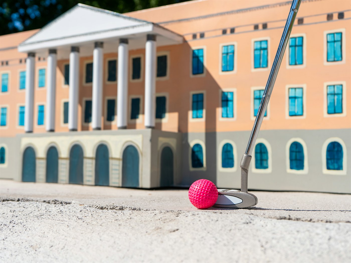 Minigolfkølle slår mot rosa ball foran  kuliss av slottet i Oslo.