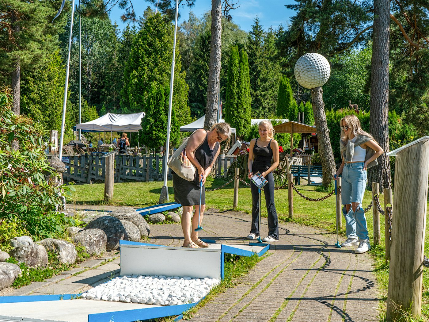 A mother and two teenage daughters smile and play miniature golf. Photo