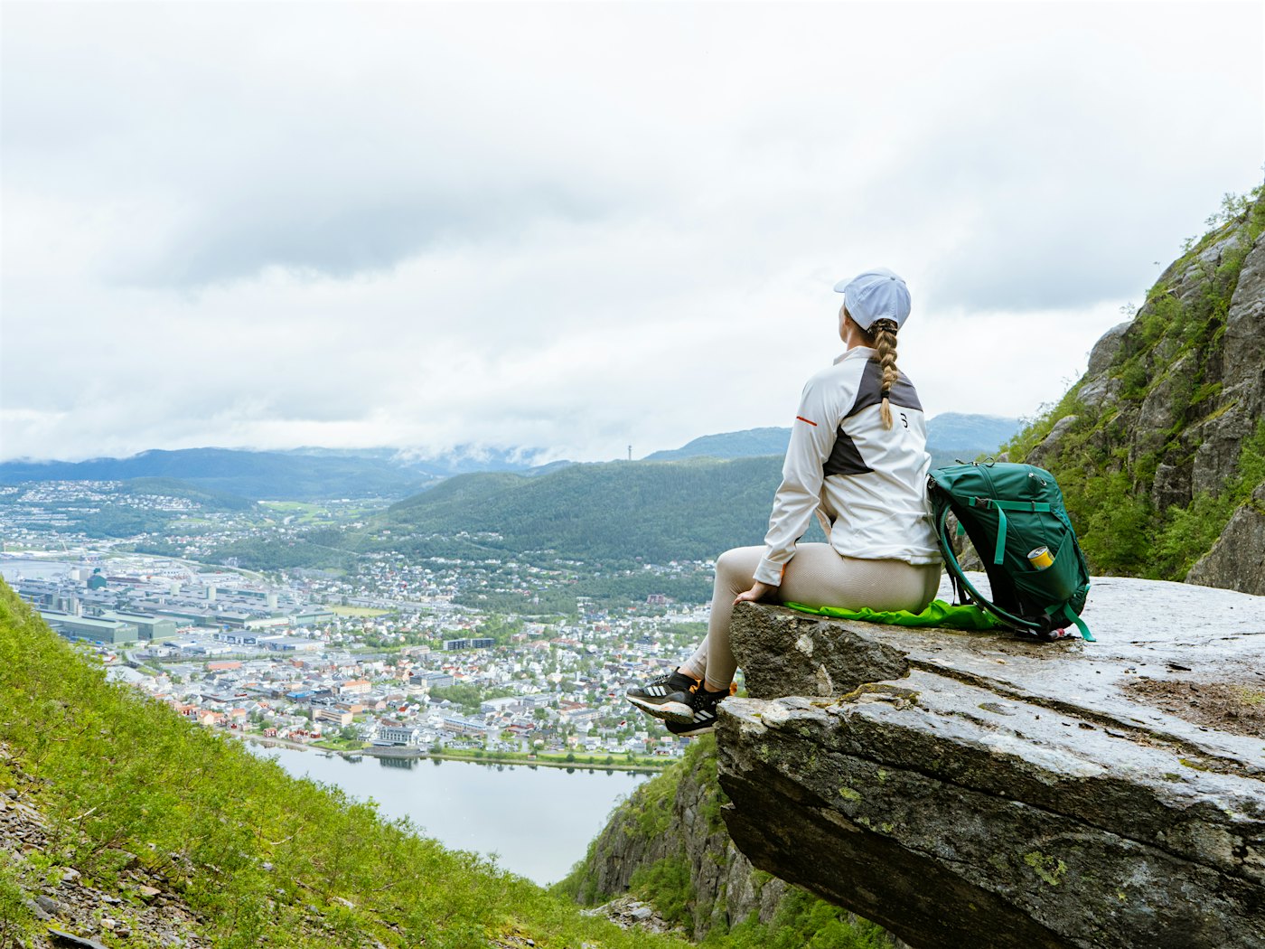 Dame sitter på fjellhylle og ser utover utsikten over fjell, fjord og Mosjøen.