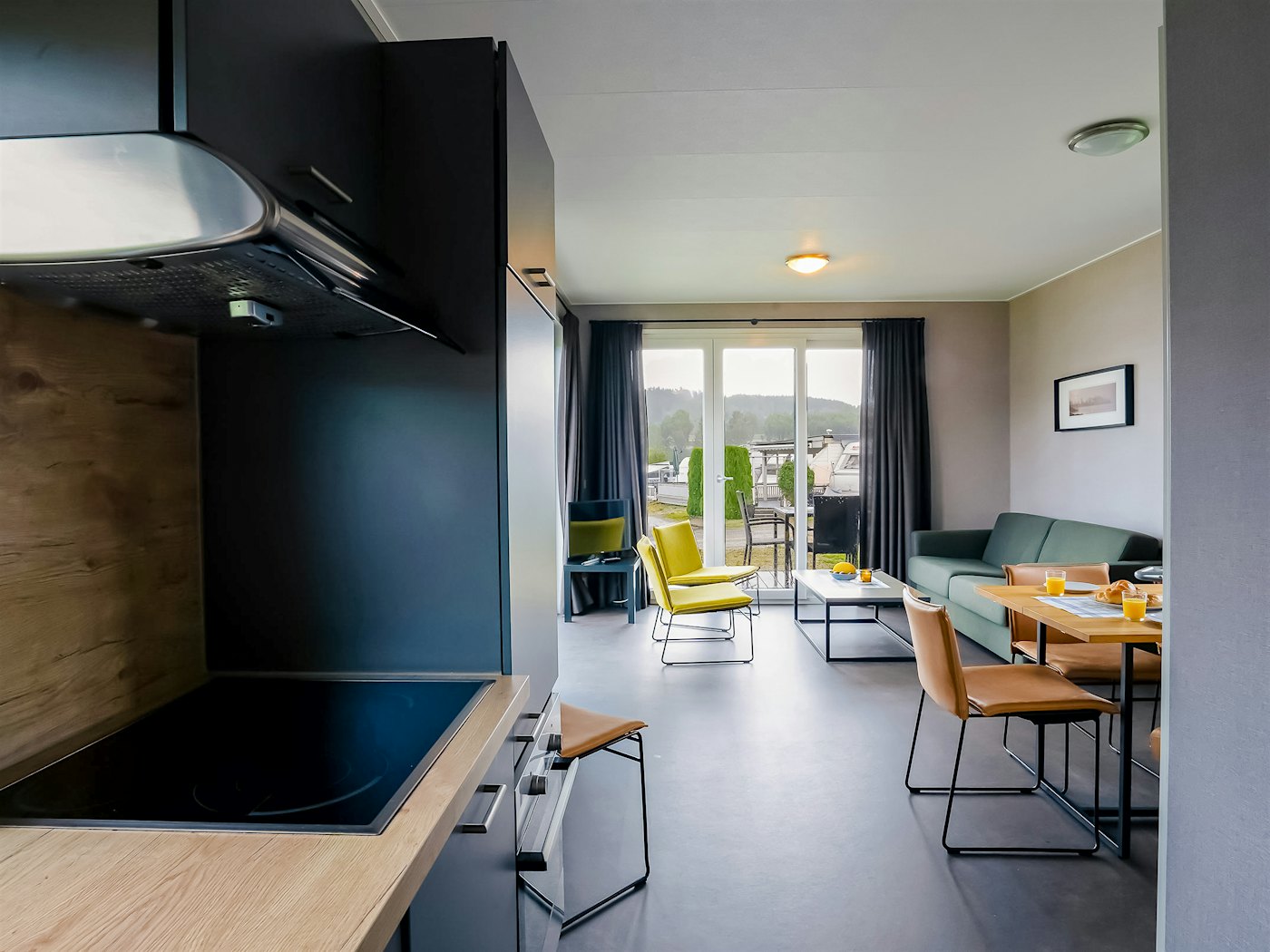 Moderne rom med kjøkken, sofa og spisebord. Vinduer fra gulv til tak. Foto