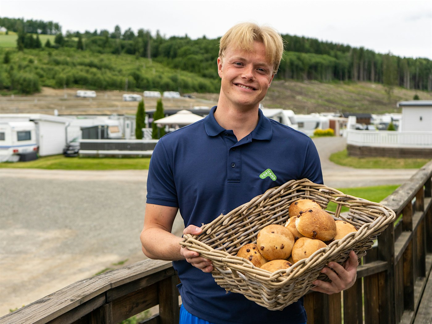 A happy youth smiles widely while holding a basket of raisin buns. Photo
