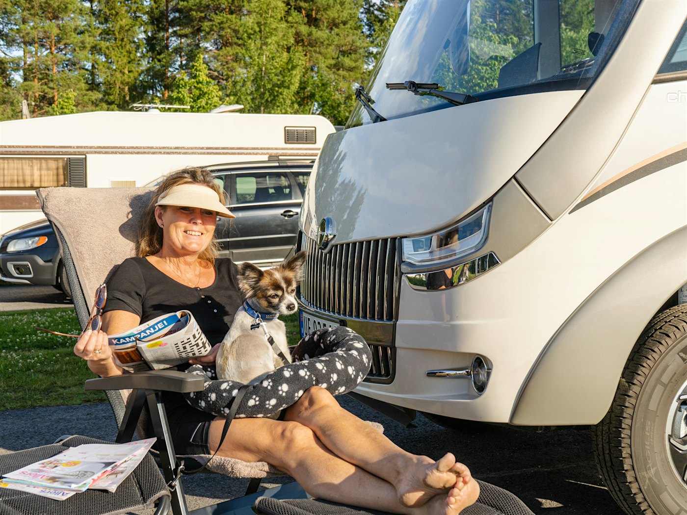 Lady reads a newspaper outside her motorhome with a dog on her lap. Photo