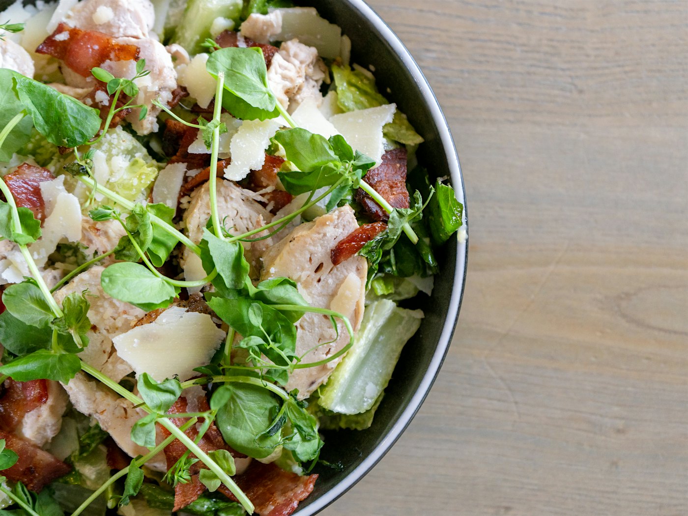 Ein Teller Caesar Salad mit Hähnchenfilet, Speck, Parmesan und Salat. Foto