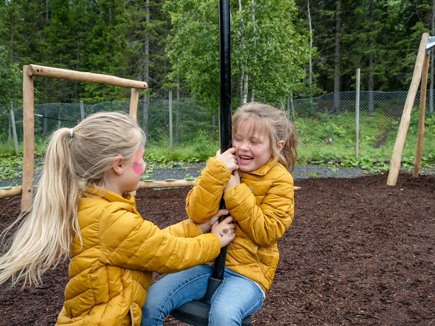 To jenter leker på zipline på lekeplass og ler.
