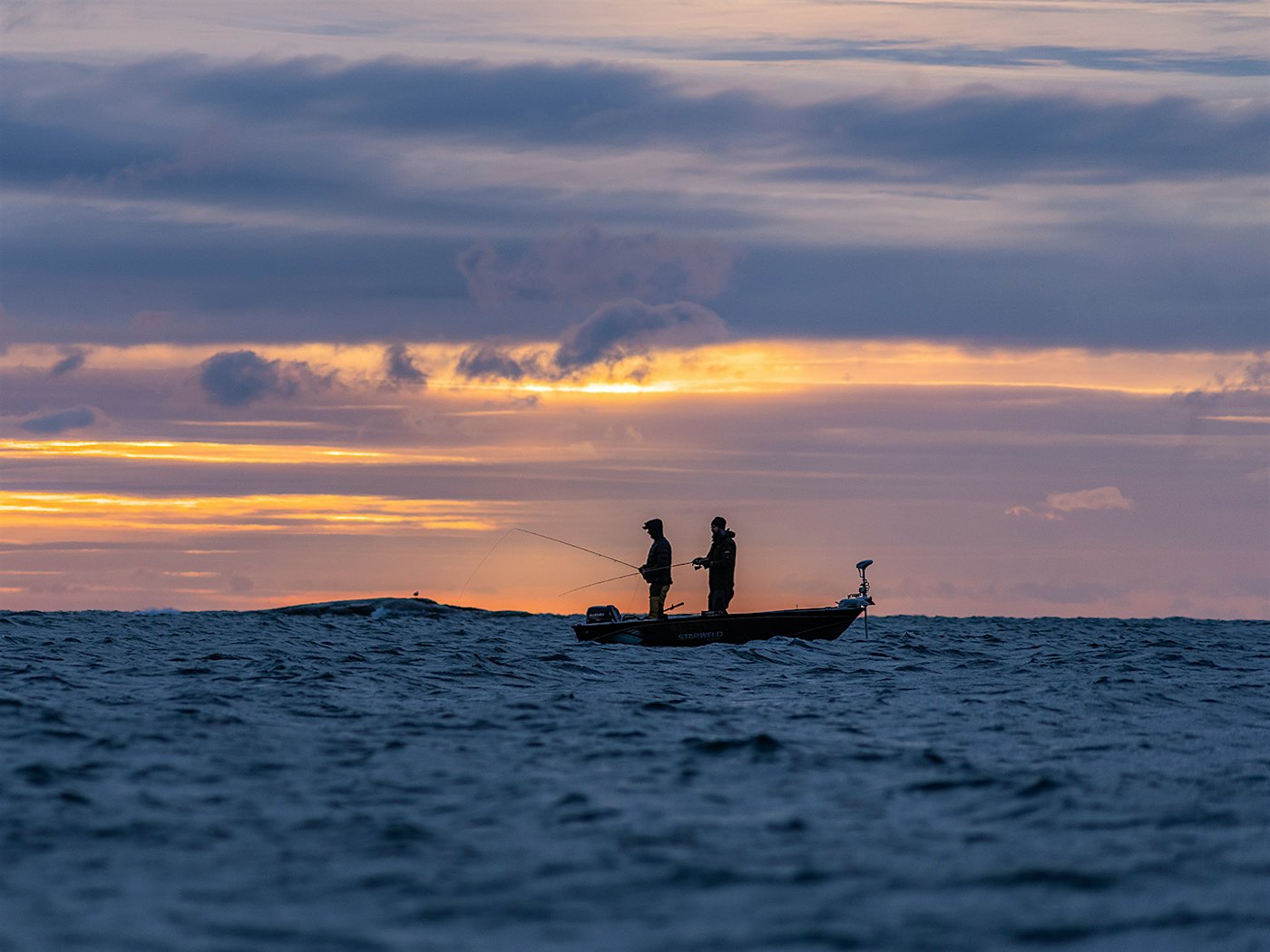 Liten båt på havet, med to fiskere i solnedgang. Foto