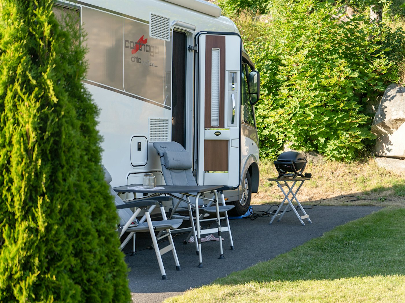 A mobile home on a pitch, with a barbecue, chairs and a table on the outside. Photo