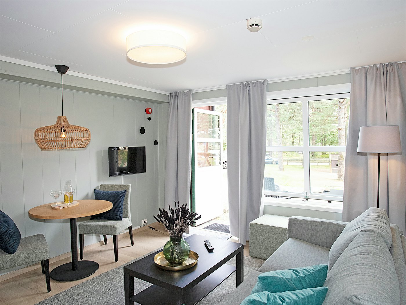Lys og moderne stue med sofa, spisebord, TV, store vinduer med lange lyse gardinger. Foto