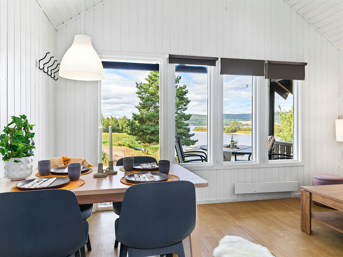Lyst rom med store vinduer, utsikt mot vannet. Spisebord er dekket til måltid. Foto