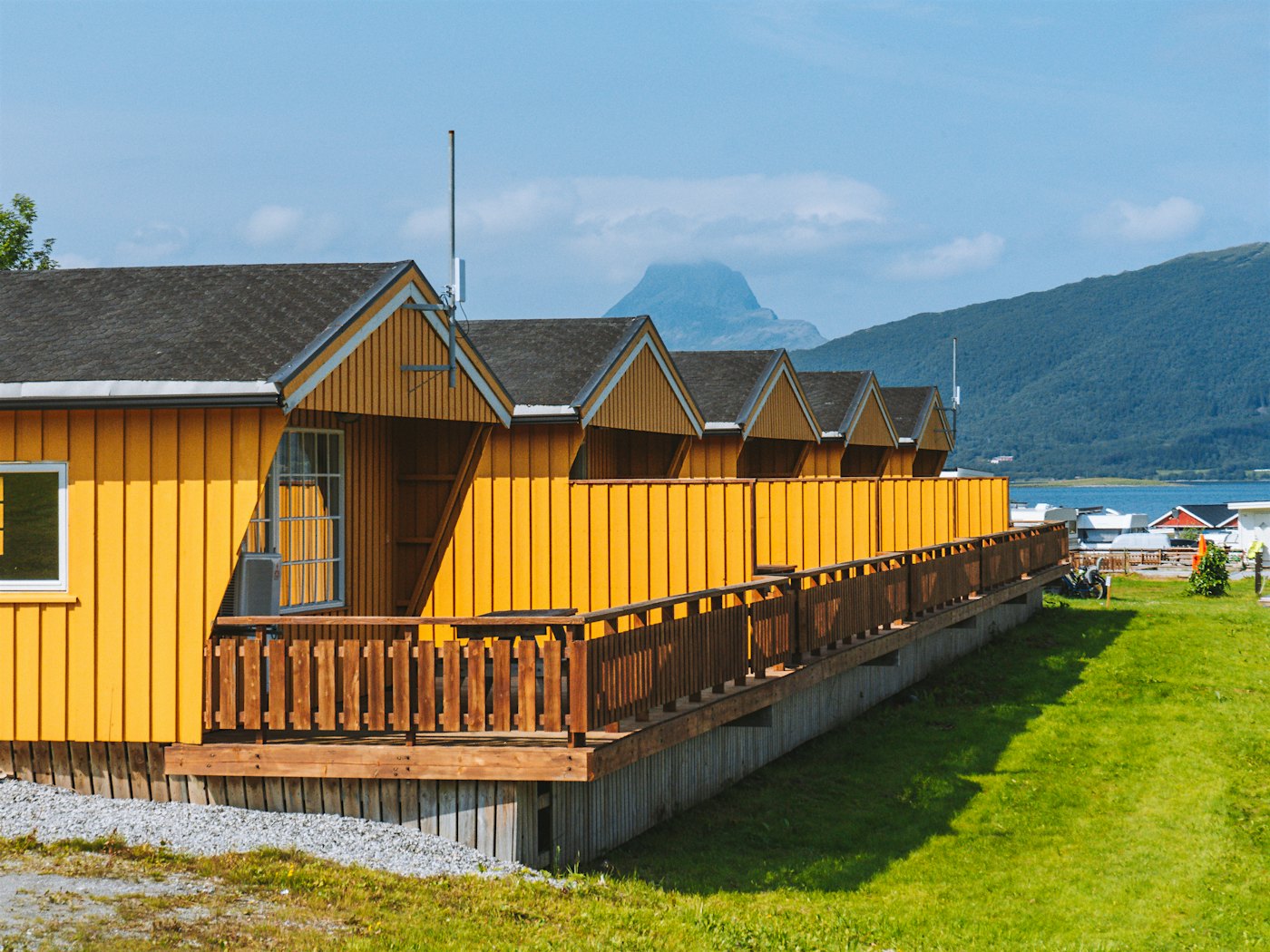 Äußeres von fünf gelben Cottages mit Terrasse. Grüner Rasen davor und Berge im Hintergrund. Foto