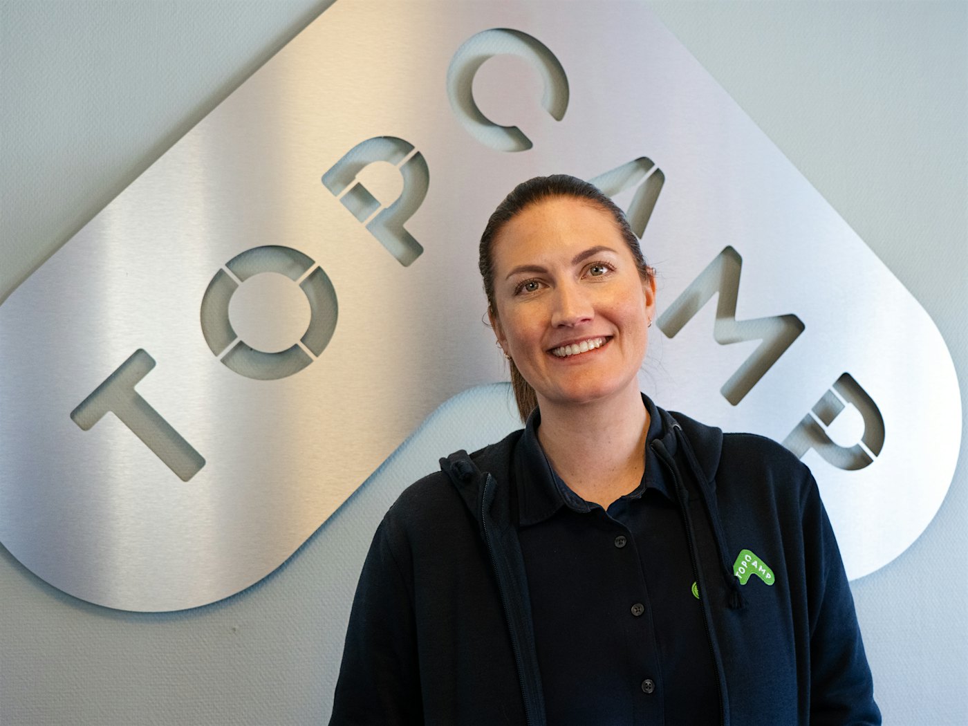 Frau lächelt breit vor Topcamp-Logo. Foto