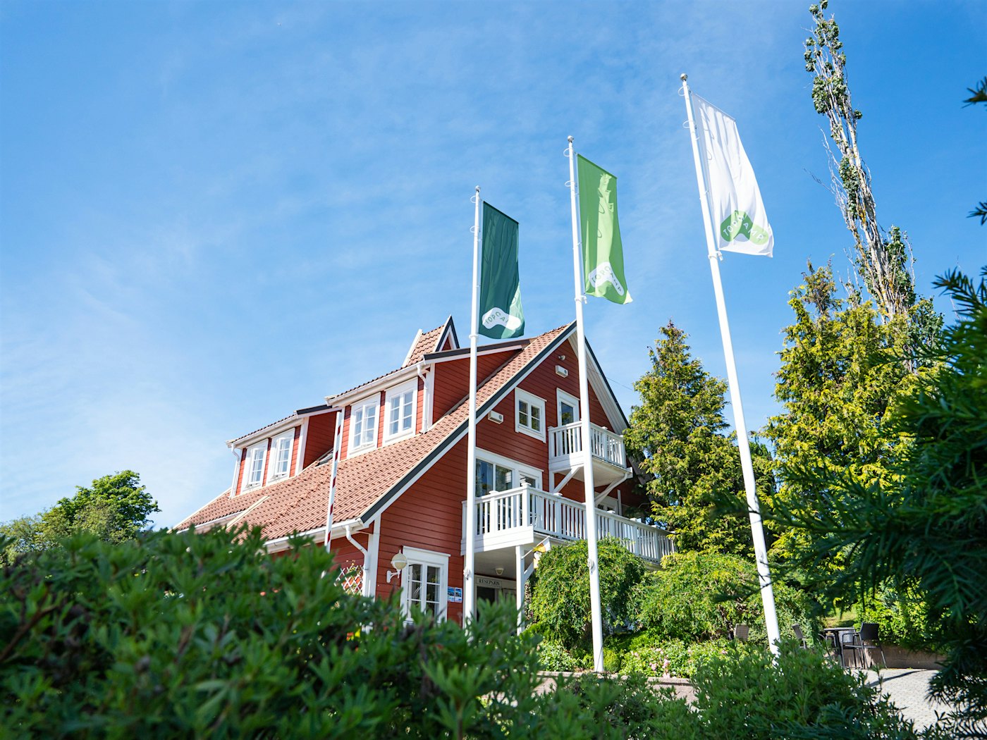 Driveway in front of the red reception building, three Topcamp flags and green trees at Topcamp Bie. Photo