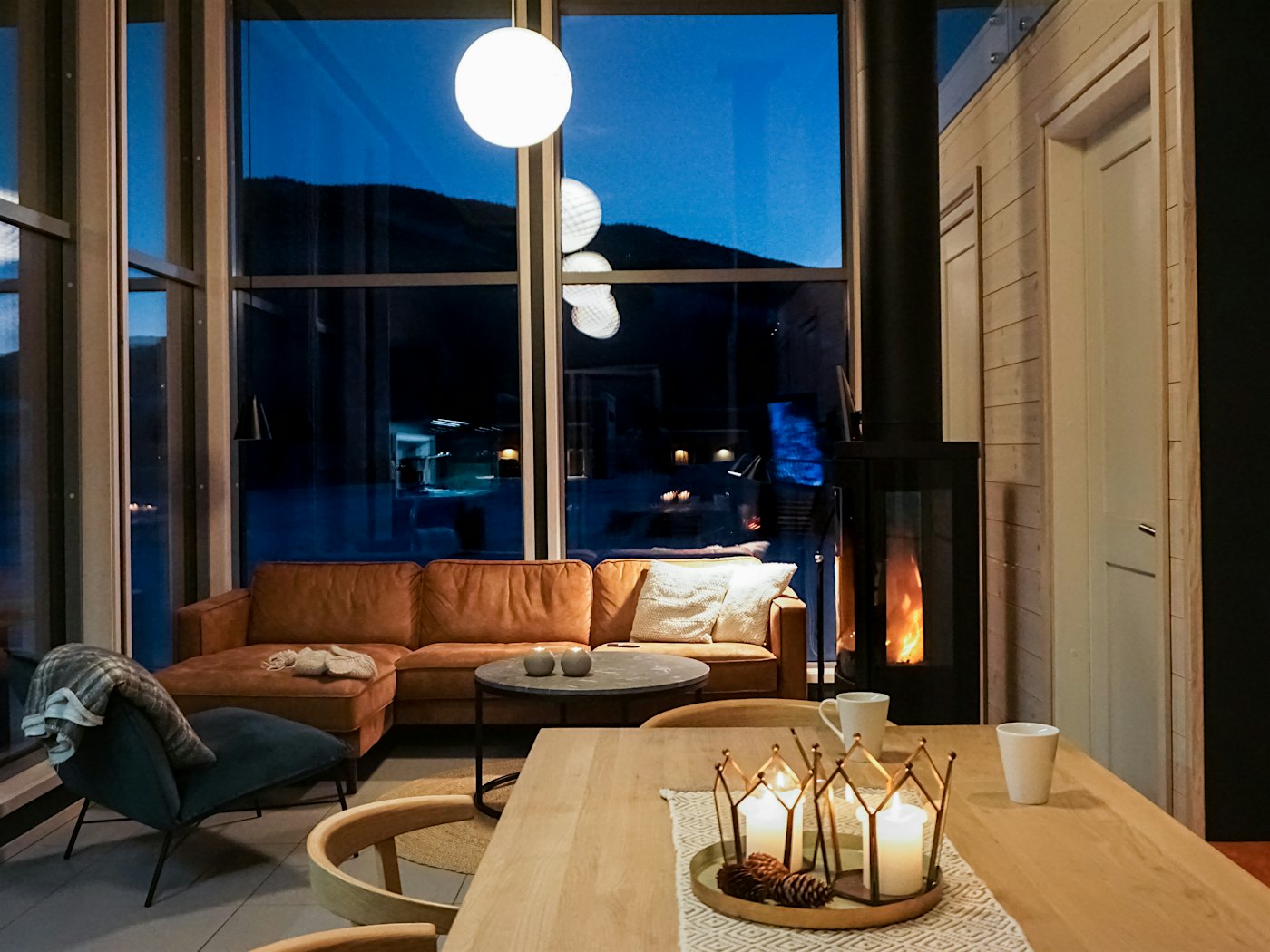 Moderne stue med sofa, sofabord, stuebord og peis. Store vinduer fra gulv til tak.