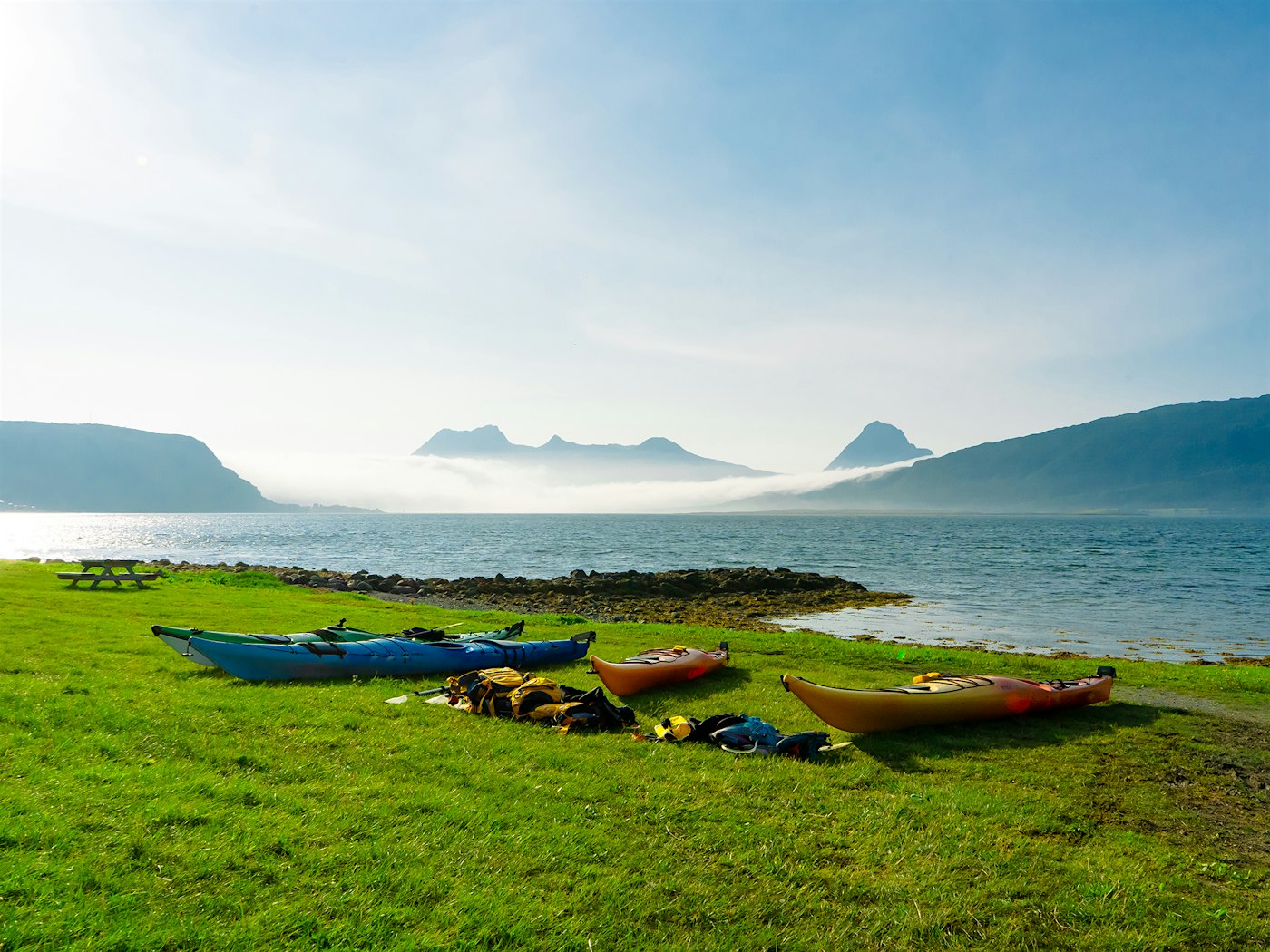 Kayaks lie on the shoreline with mountains in the background. Photo