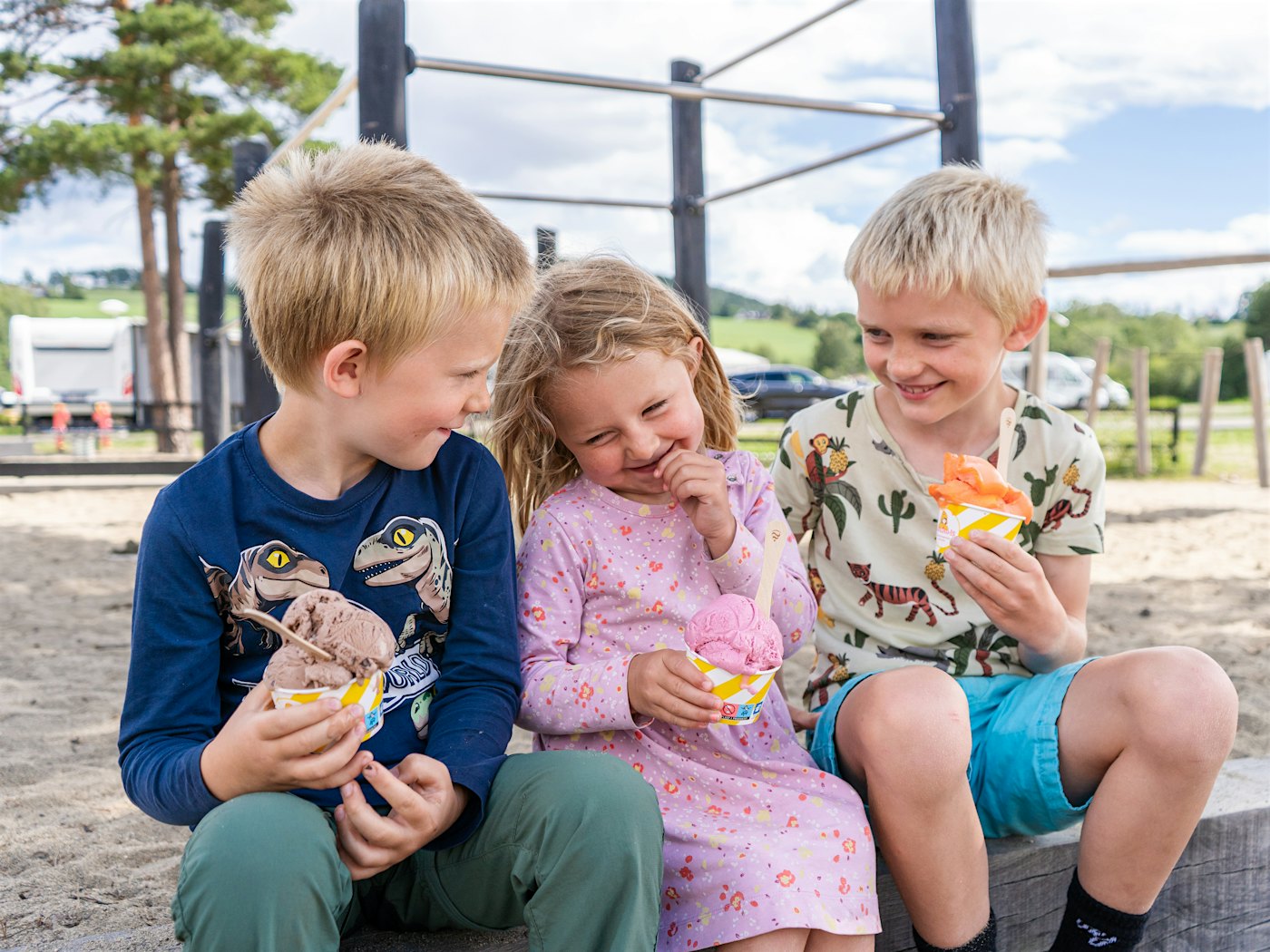 Zwei Jungen und ein Mädchen sitzen auf einem Spielplatz und essen Eis. Foto